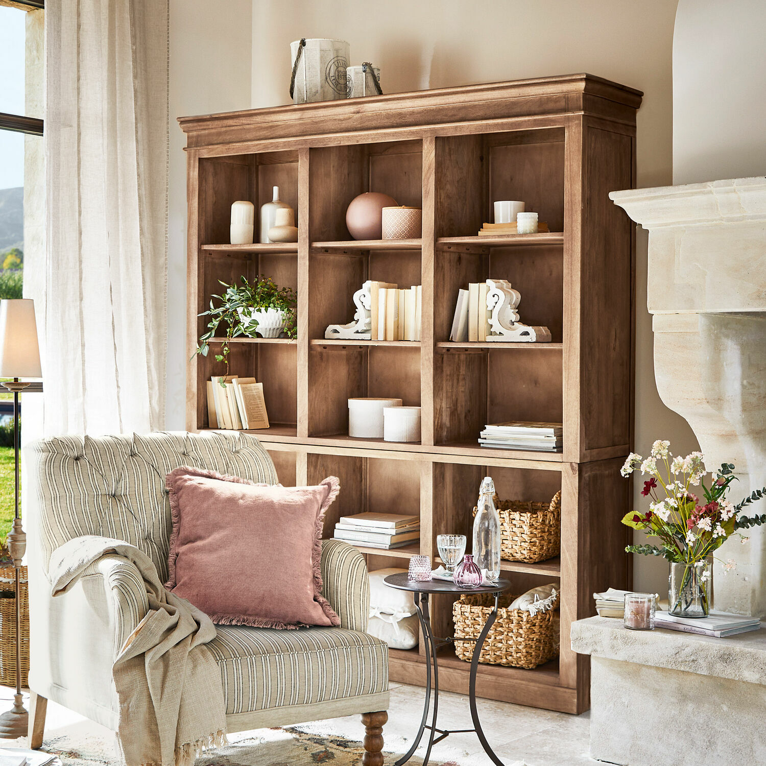 Helles braunes Holzregal mit Dekorationen und Büchern in gemütlichem Wohnzimmer mit gestreiftem Sessel