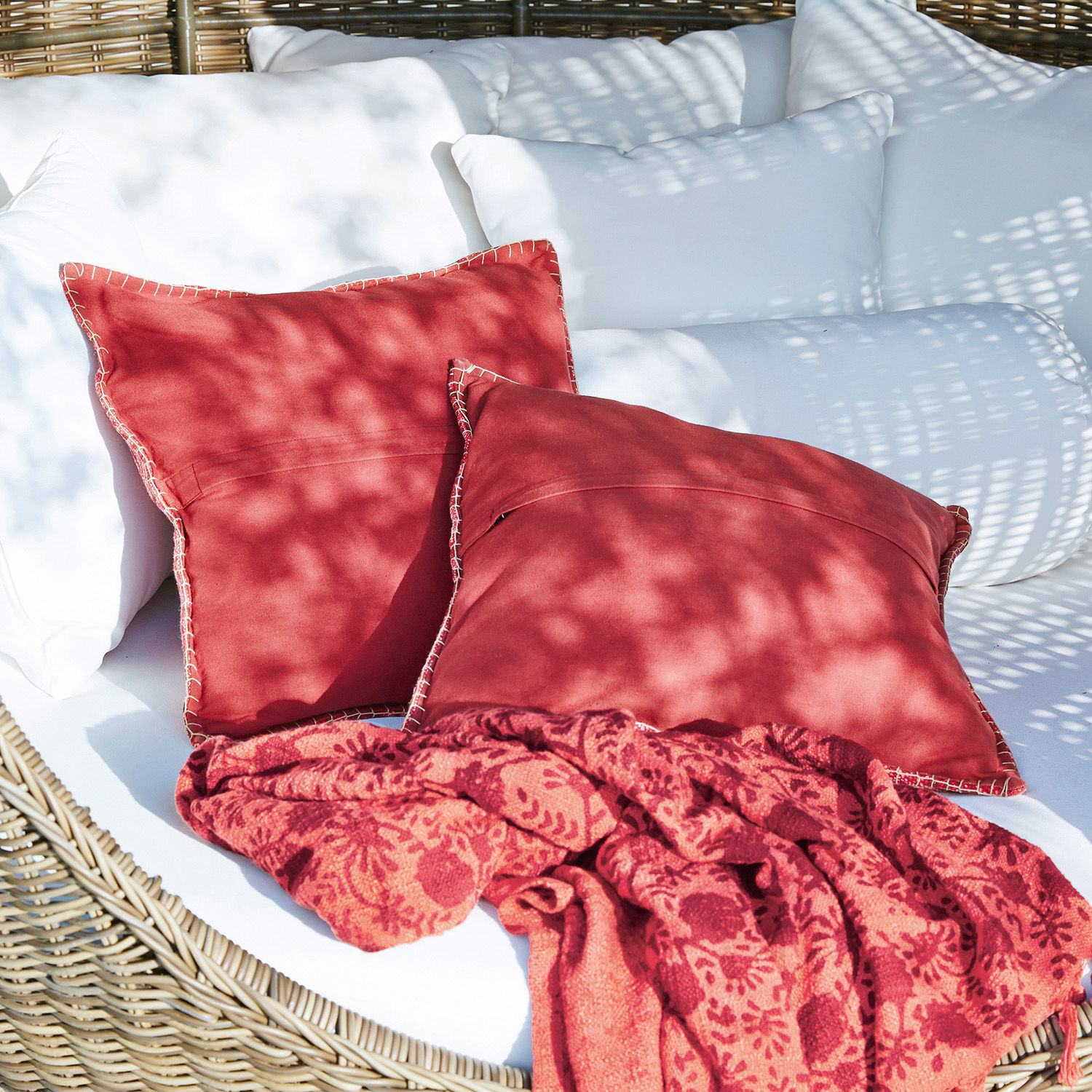 Rote Baumwollkissen und gemusterte Decke auf weißem Rattansofa für den Garten