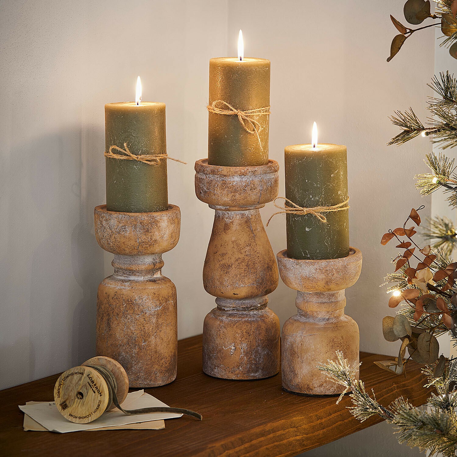 Kerzenständer 3er Set Talona Drei rustikale Holzkerzenhalter mit grünen Kerzen und Juteschnur auf dekorativem Holzregal