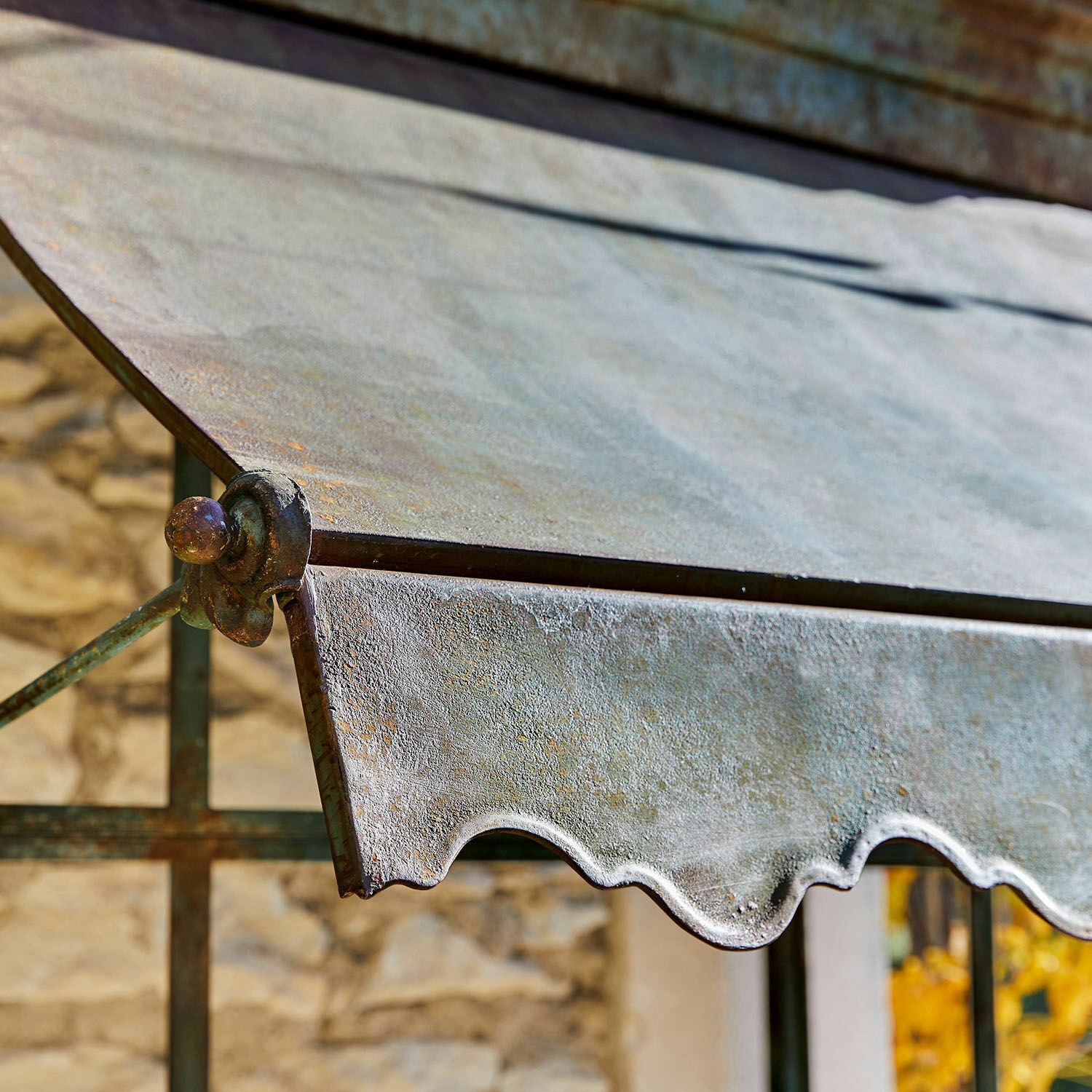 Metallvordach mit gealterter Patina und dekorativem wellenförmigem Rand vor Steinmauer
