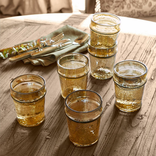 Sechsteiliges Set bernsteinfarbener Gläser auf Holztisch mit Serviette und Besteck