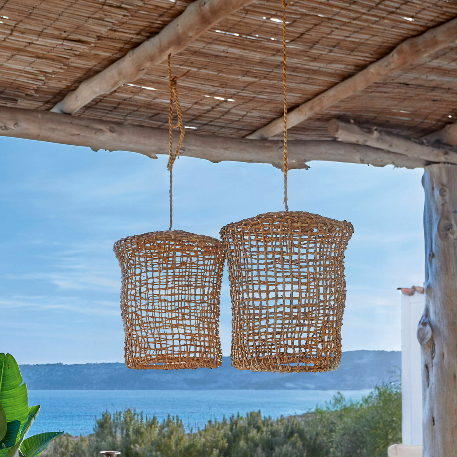 Zwei hängende Lampions aus natürlichem braunem Rattan vor Meerblick, stilvolle Outdoor-Dekoration