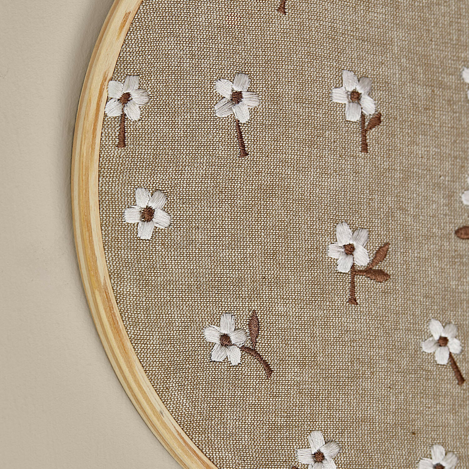 Runder heller Holzrahmen mit beigem Stoff und weißen bestickten Blumen, dekorative Wandgestaltung