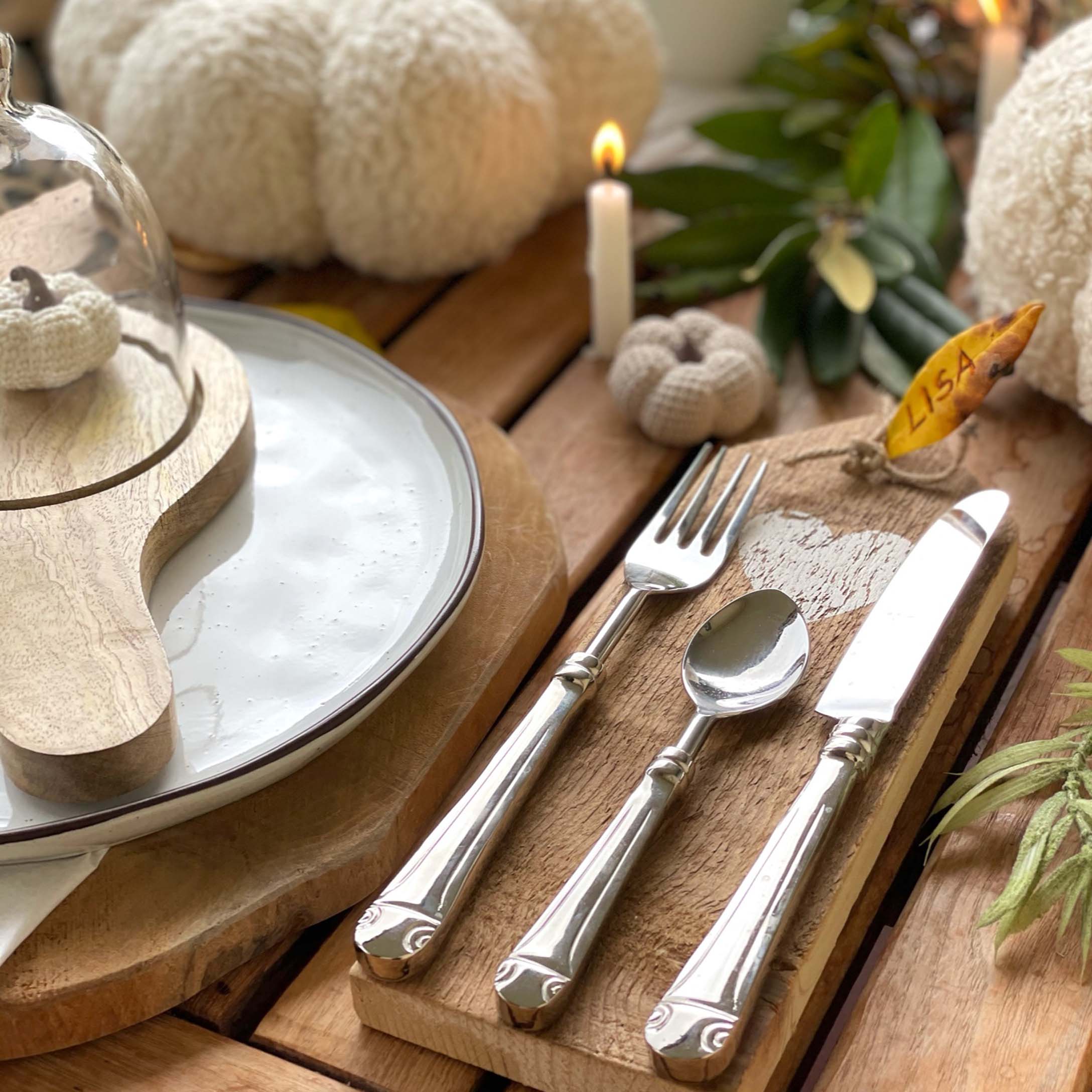 Rustikaler Holztisch mit herbstlicher Dekoration, silbernes Besteck und weiße gehäkelte Kürbisse