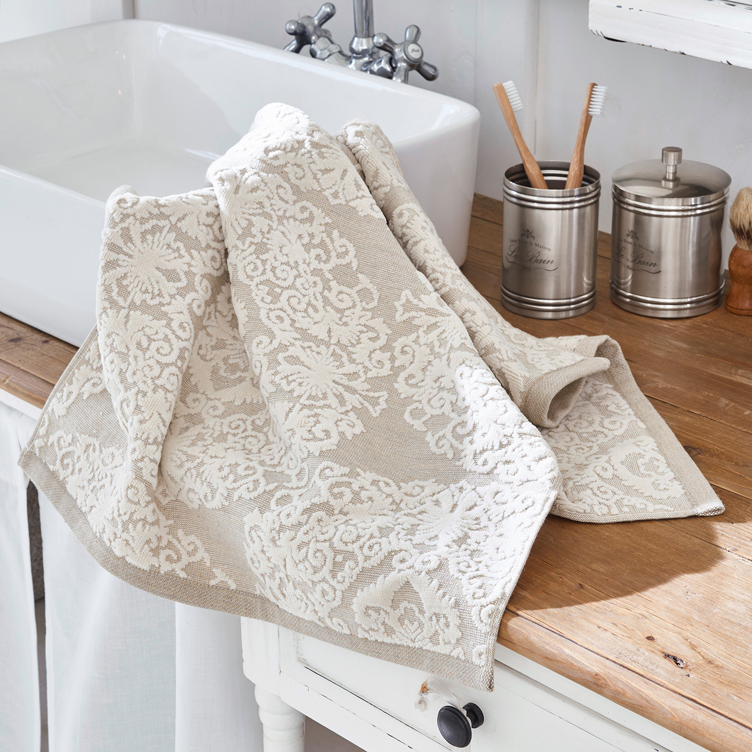 Beige Baumwollhandtuch mit weißem Muster auf Holzablage neben Waschbecken, Badezimmerzubehör