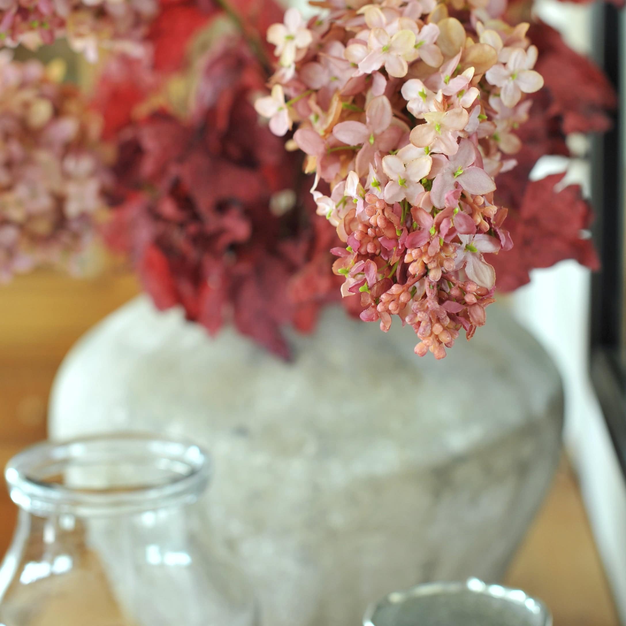 Dekorative rosa Blüten in grauer Keramikvase auf Holztisch als Wohnaccessoire