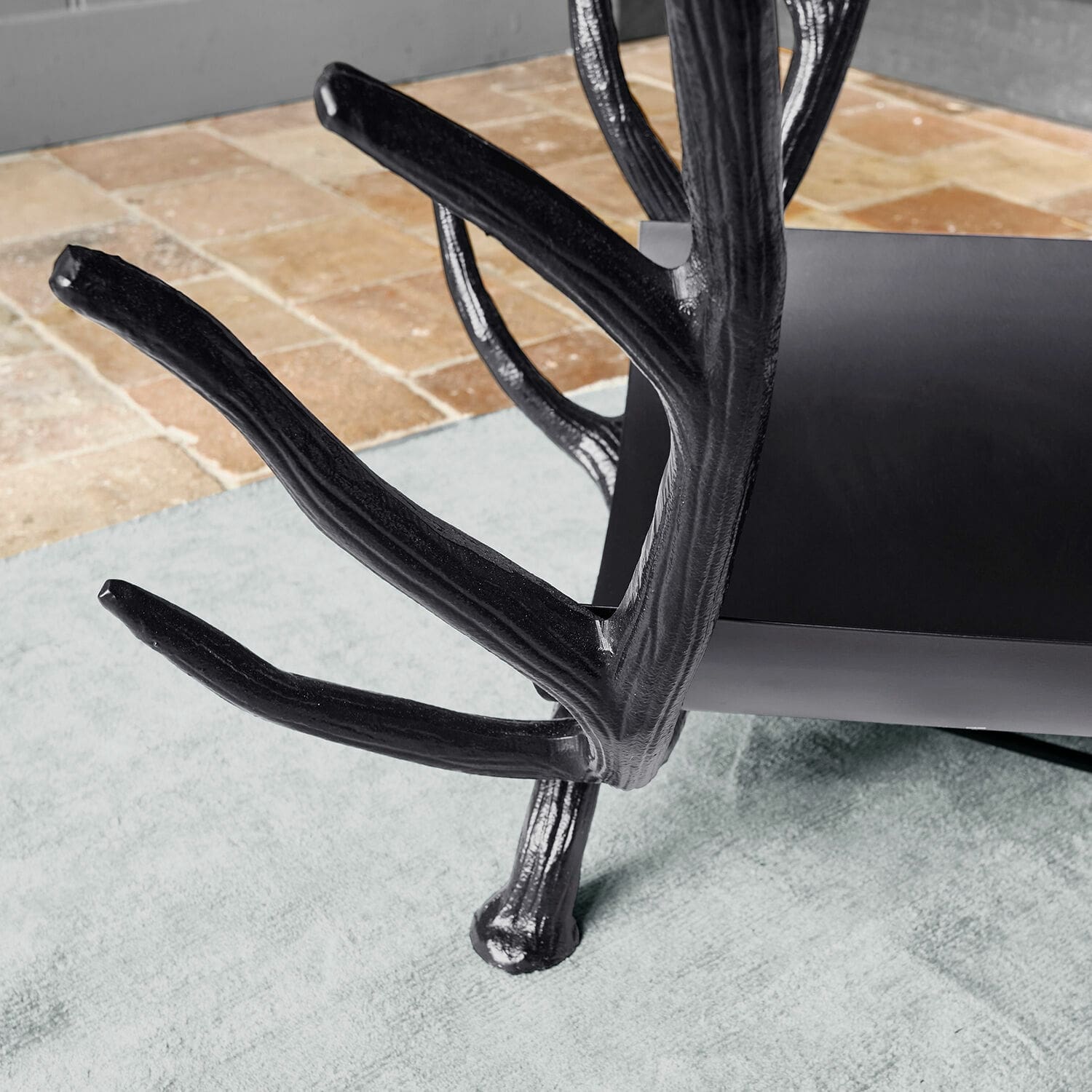 Schwarzer Metall-Couchtisch mit astförmigen Beinen auf hellem Teppich und Fliesen, modernes Design