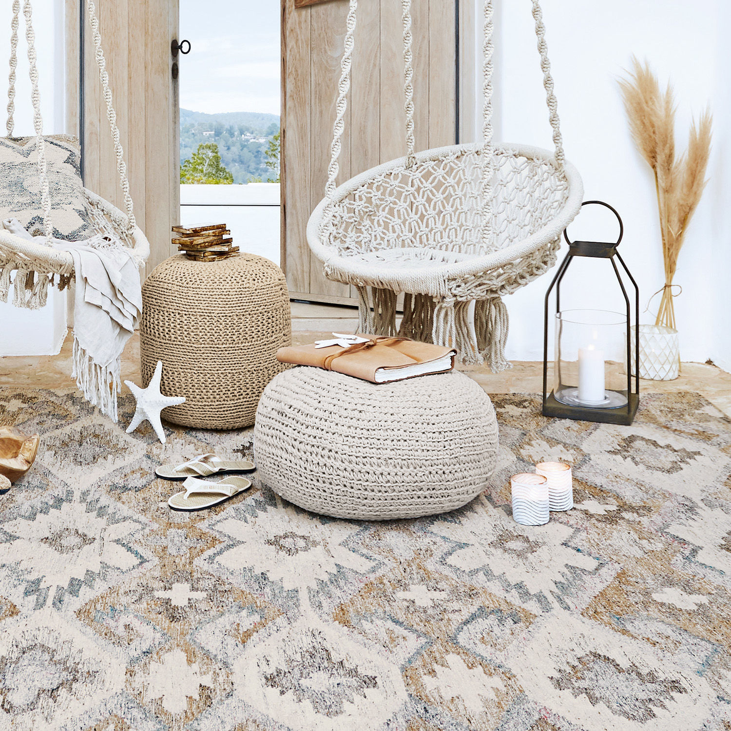 Gemütliches Wohnzimmer mit weißem Makramee-Hängesessel und beigen gestrickten Poufs auf gemustertem Teppich