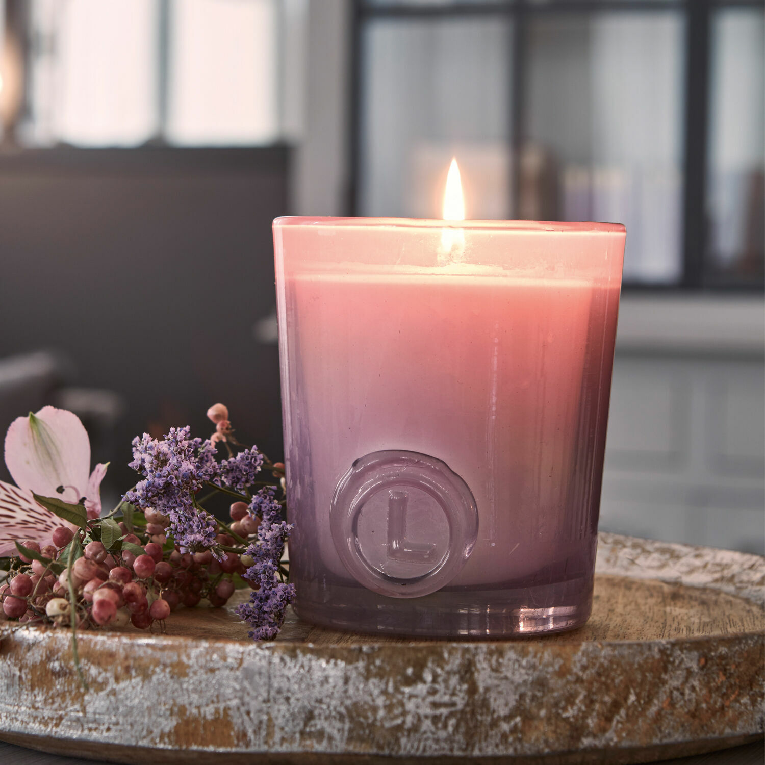 Rosa Duftkerze im Glas auf Holztablett mit Blumen, stilvolle Wohnraumdekoration