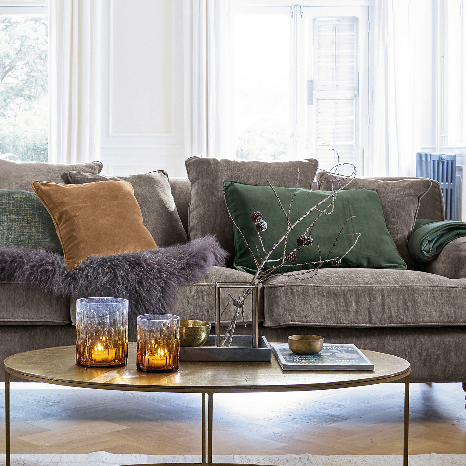 Graues Sofa mit grünen und braunen Kissen, goldener Couchtisch mit Dekorationen und brennenden Kerzen