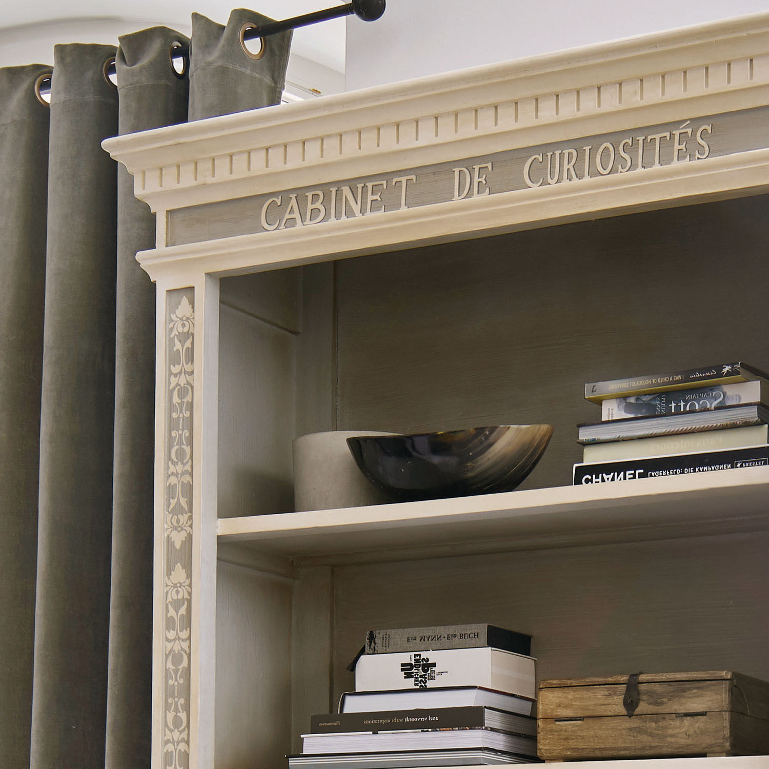 Beige Holzregal mit Schriftzug Cabinet de Curiosités, dekorativen Mustern, Büchern und Holzkiste