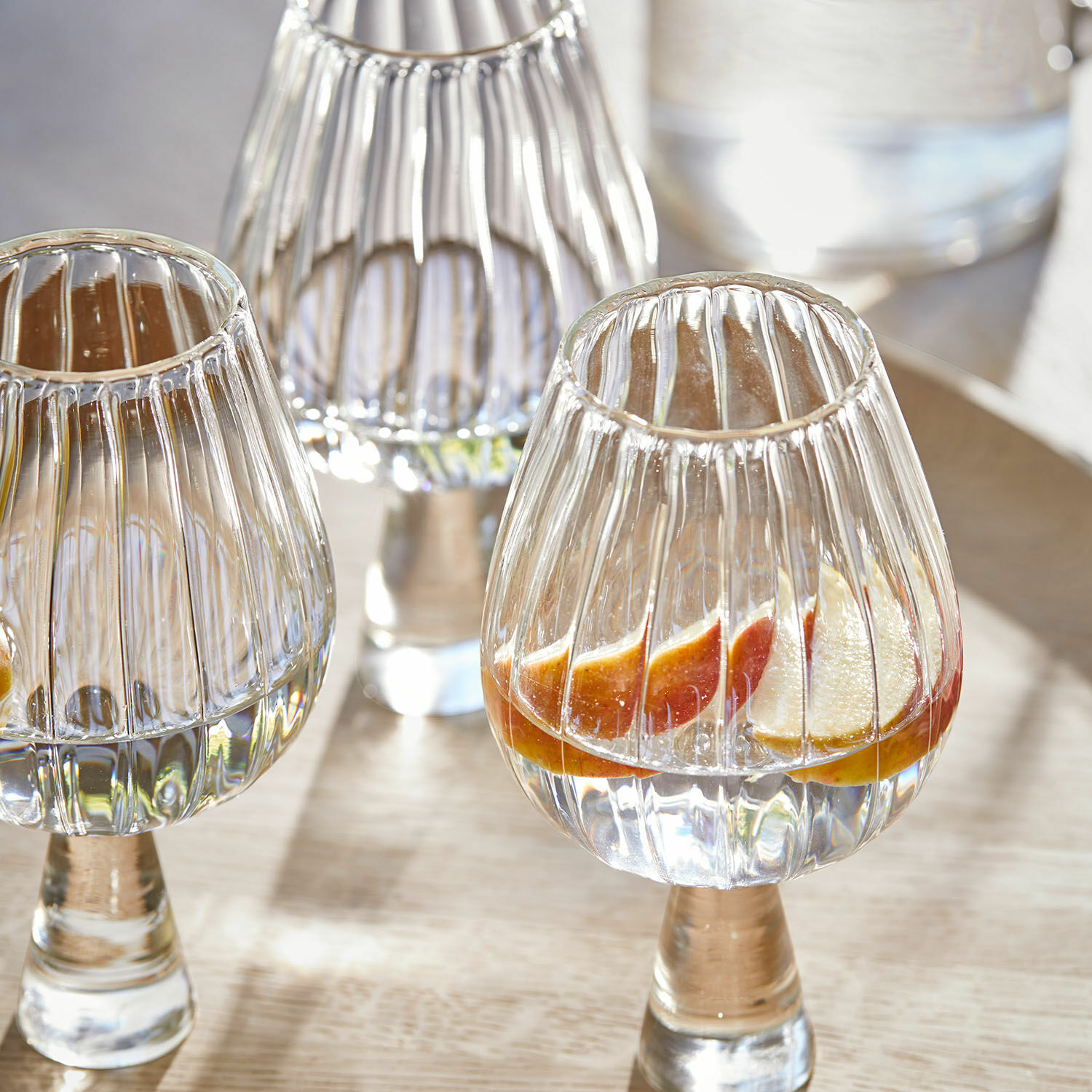 Gläser aus geriffeltem klarem Glas auf Fuß mit Fruchtscheiben und Wasser auf Holztisch