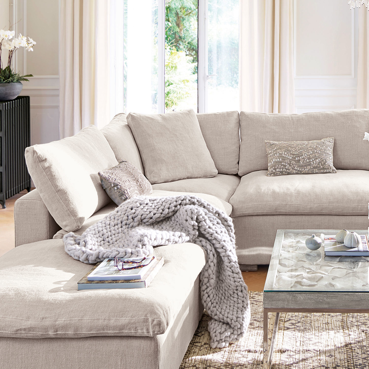 Sessel Bennington Corner Beige Ecksofa aus Stoff mit Kissen und grauer Strickdecke in hellem Wohnzimmer