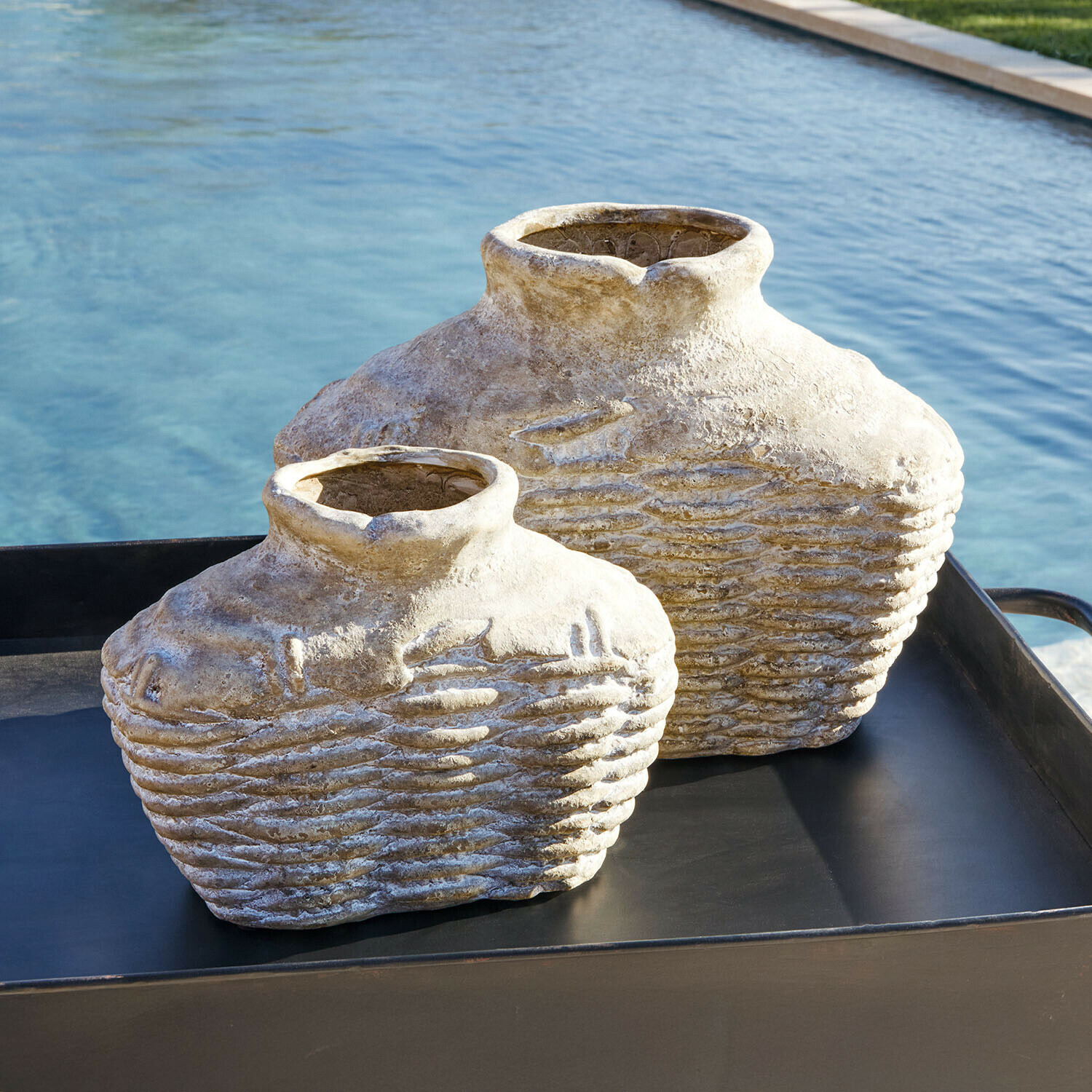Zwei dekorative beige Steinvase auf schwarzem Tablett neben einem Pool