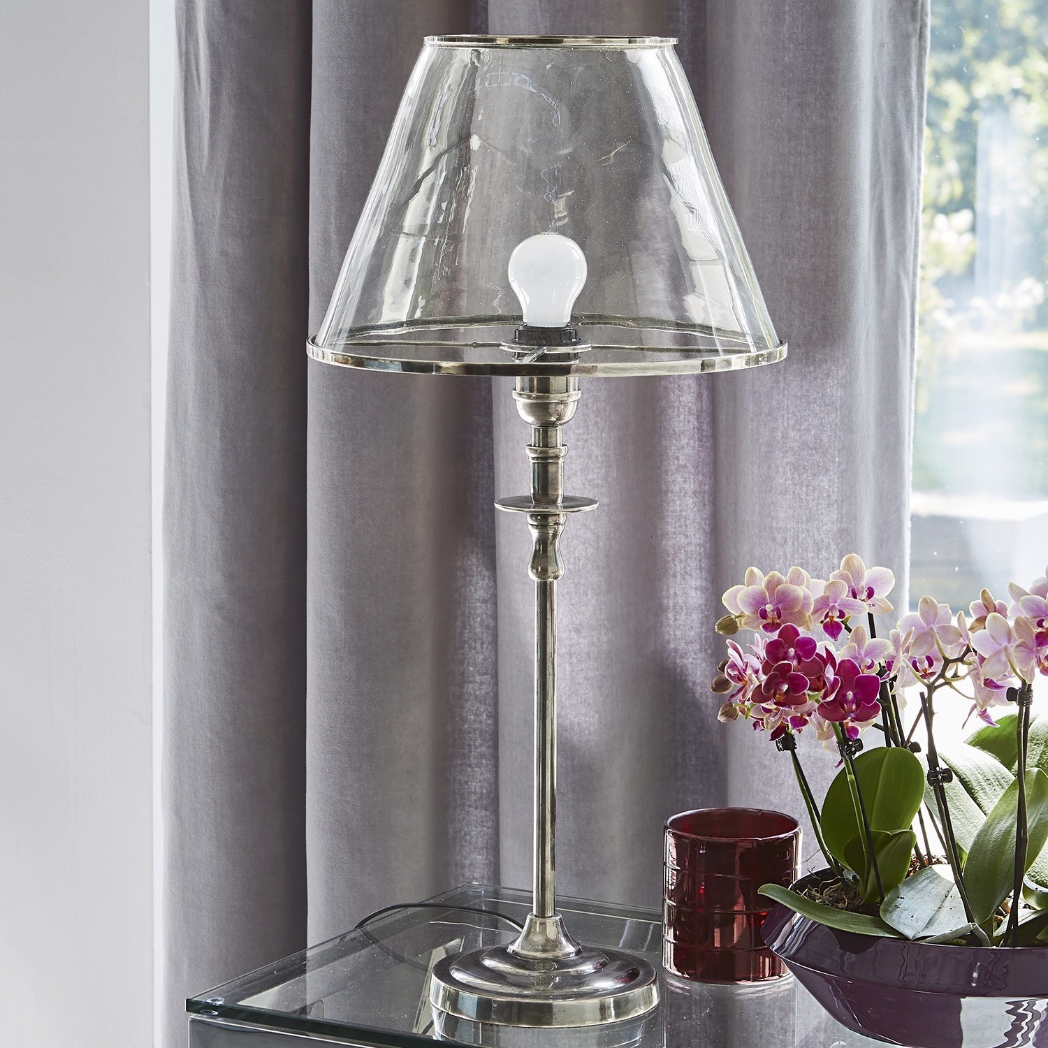 Elegante Tischlampe aus silbernem Metall mit transparentem Glasschirm auf Glastisch