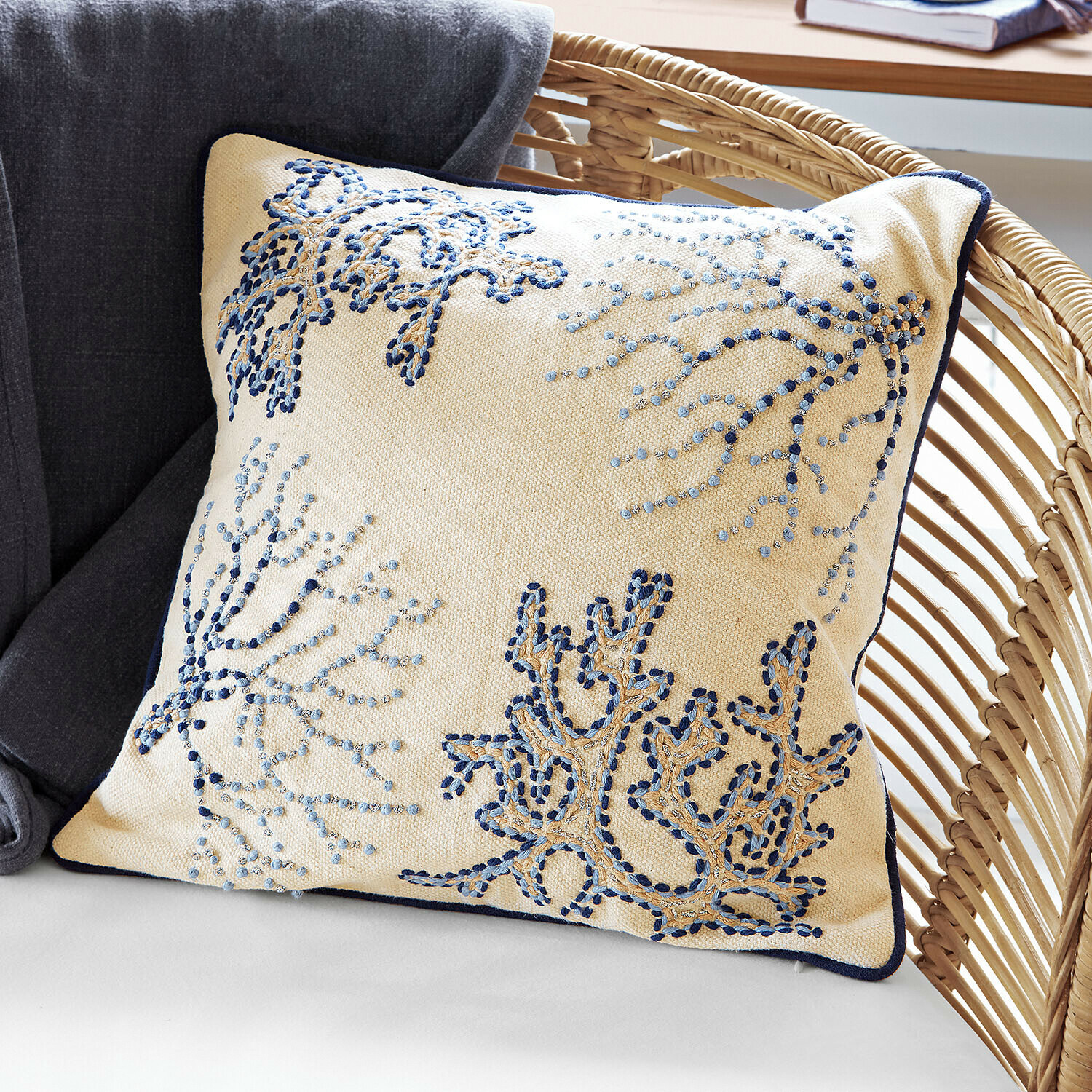 Beiges Dekokissen mit blauer Stickerei und dunkelblauem Rand auf Rattansessel