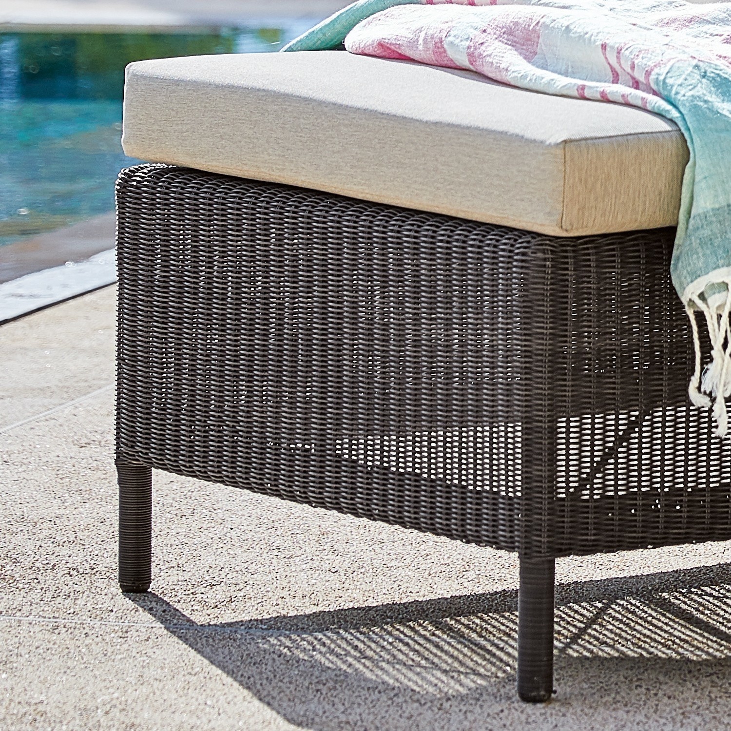 Braunes Rattan-Gartenmöbel mit beigem Polster und buntem Plaid am Poolrand