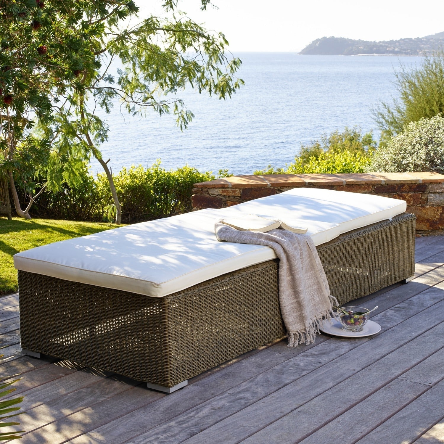 Gartenliege aus braunem Rattan mit weißer Polsterung auf Terrasse mit Meerblick