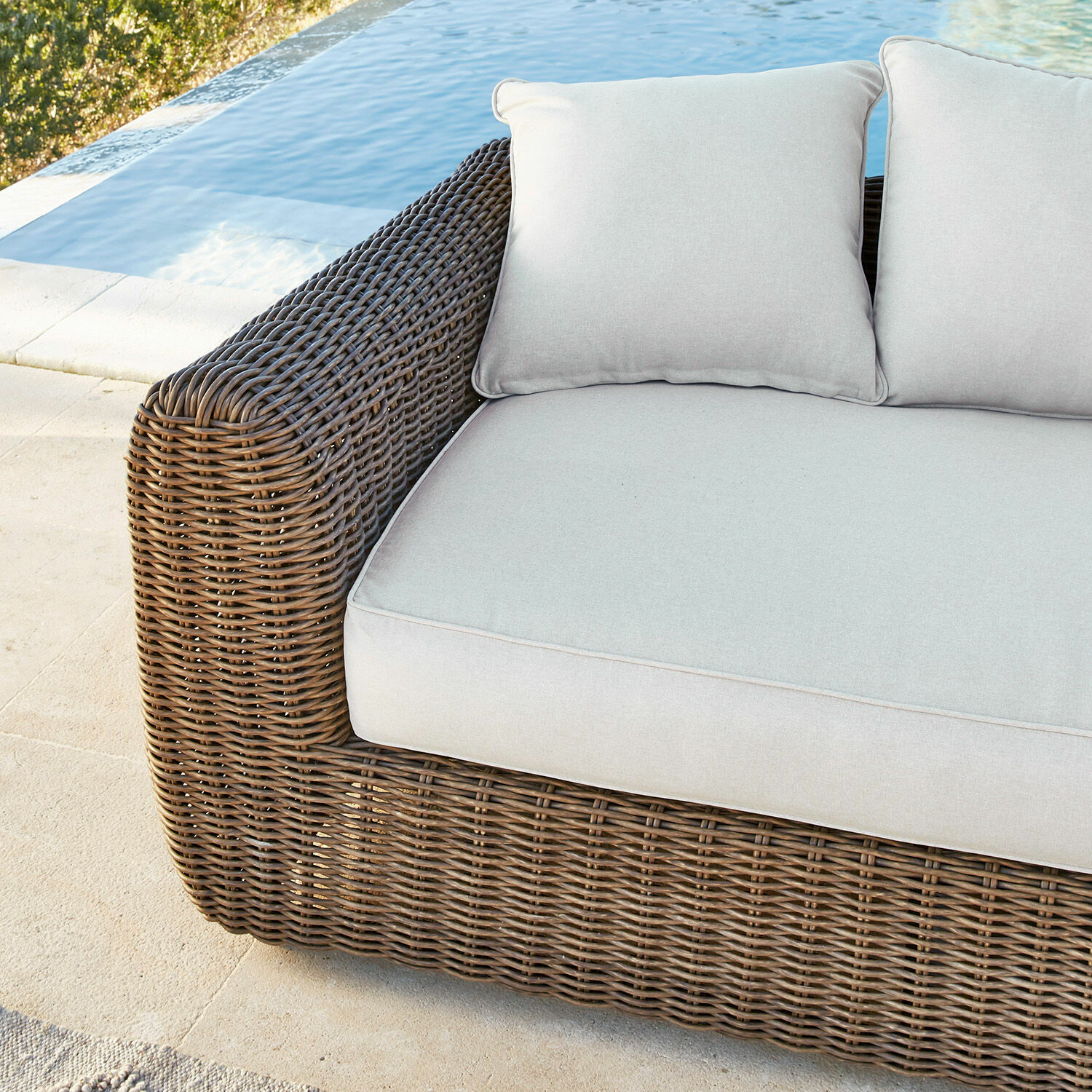 Braunes Rattan-Sofa mit hellgrauen Kissen am Pool, komfortable Gartenmöbel