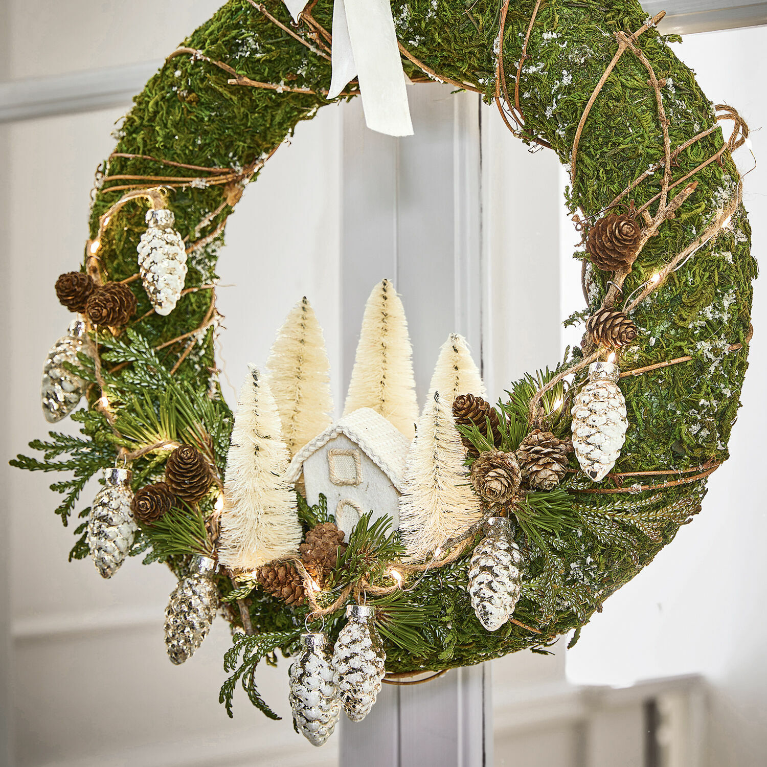 Weihnachtlicher Mooskranz mit weißen Dekorationen und Zapfen, festlicher Türschmuck für Weihnachten