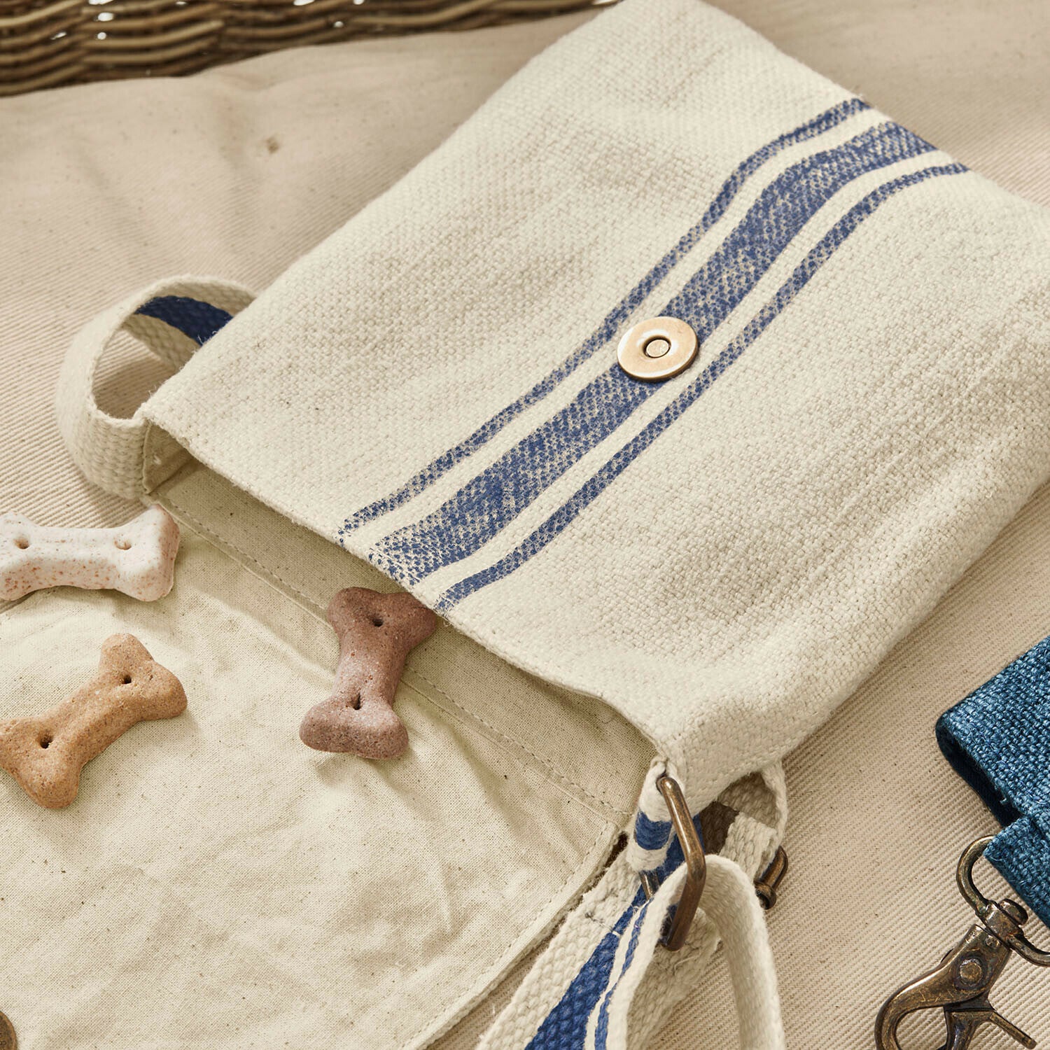 Beige Baumwolltasche mit blauen Streifen und Metallverschluss, gefüllt mit Hundekeksen