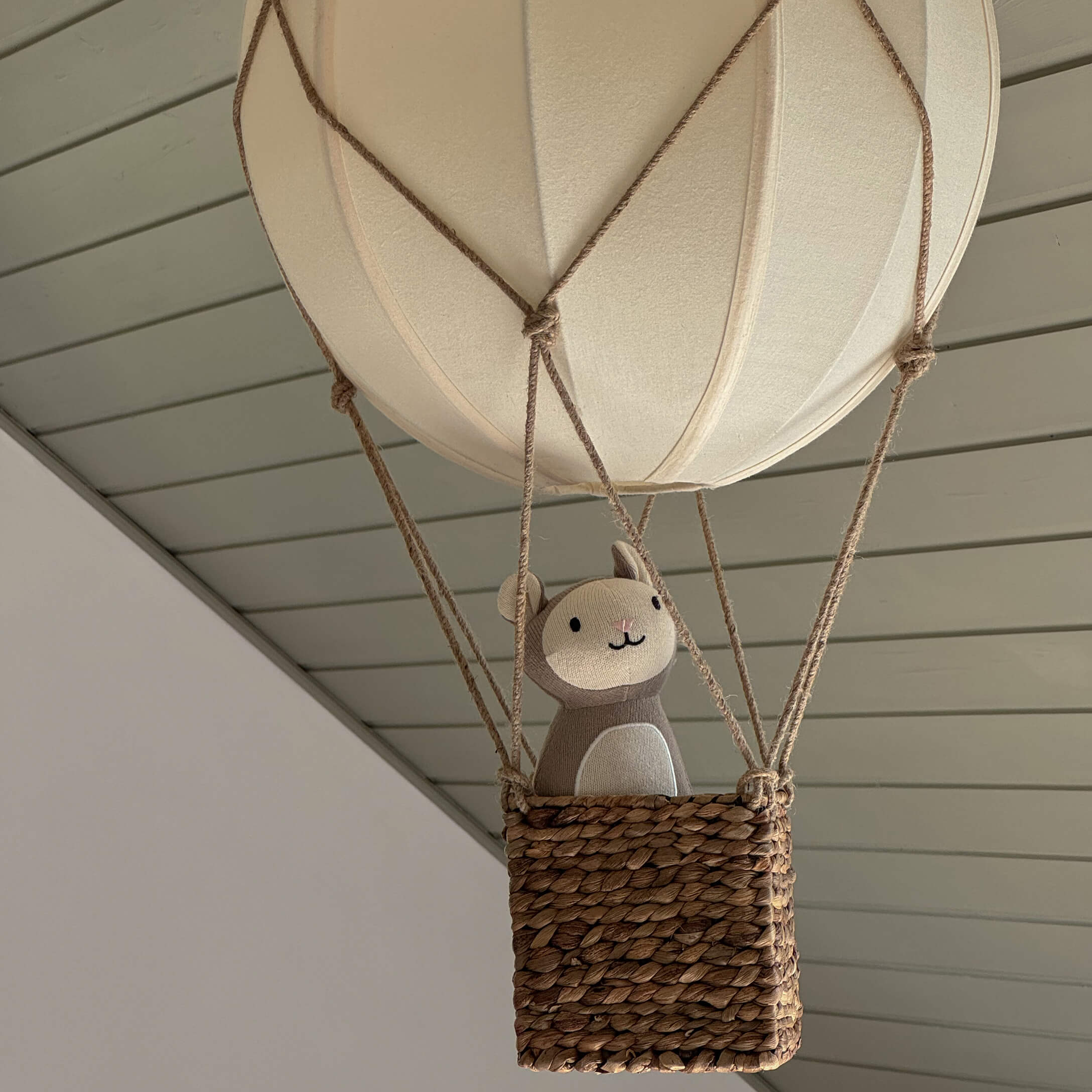 Dekorativer hängender Ballon mit Korb aus Weide und beigem Plüschtier in modernem Raum