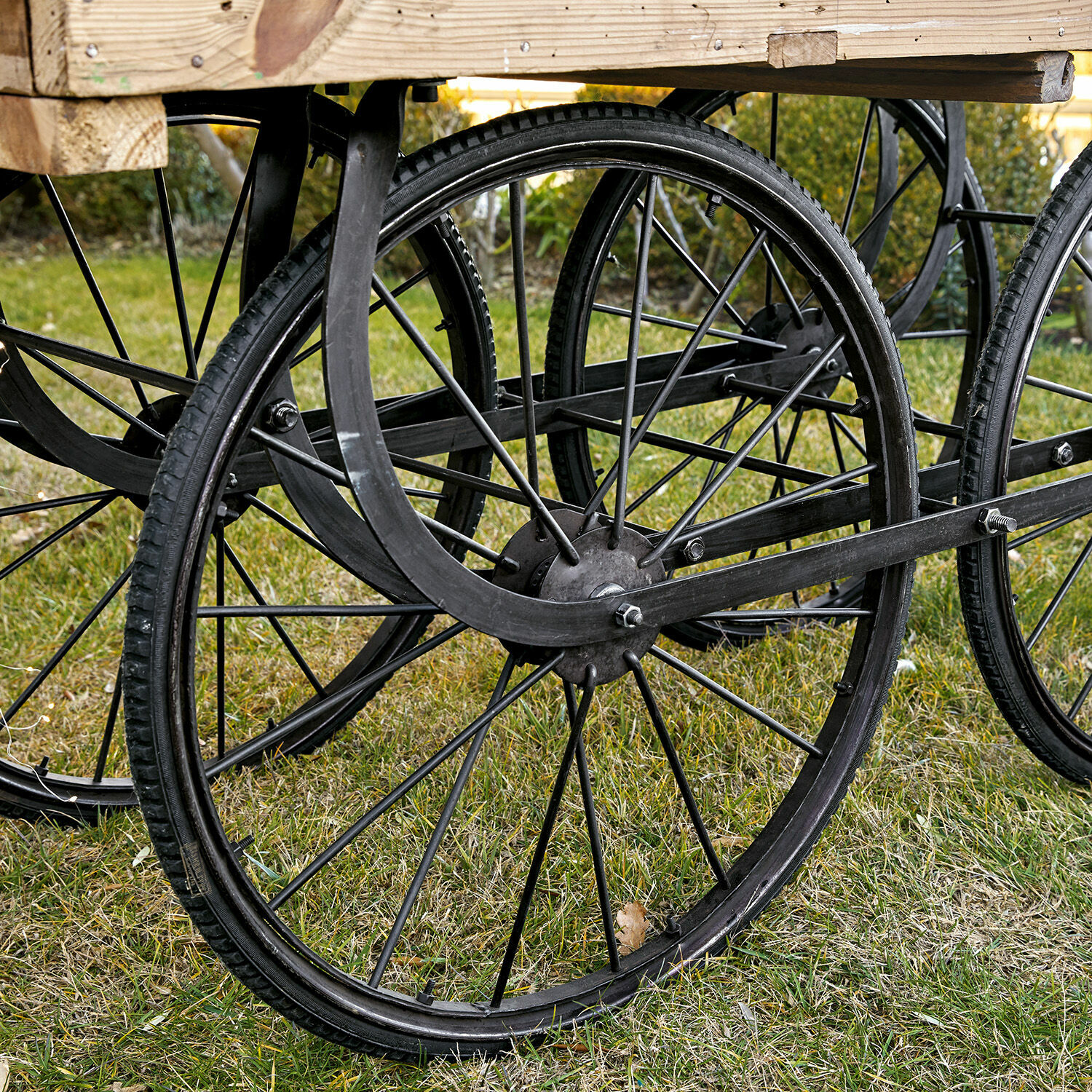 Schwarze Metallräder mit Reifen unter einer Holzplattform auf Gras, Gartendekoration