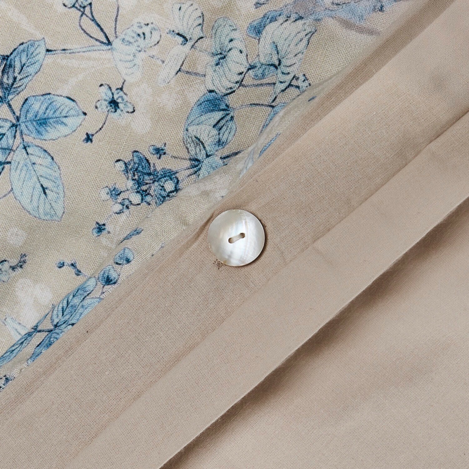 Beiger Leinenstoff mit Perlmuttknopf und blauem Blumenmuster auf natürlichem Material