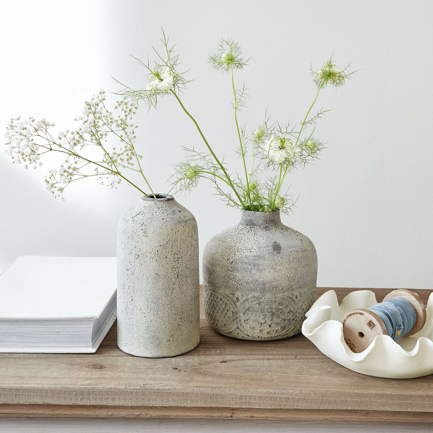 Zwei graue Keramikvasen mit zarten weißen Blumen auf hellem Holztisch dekorativ arrangiert