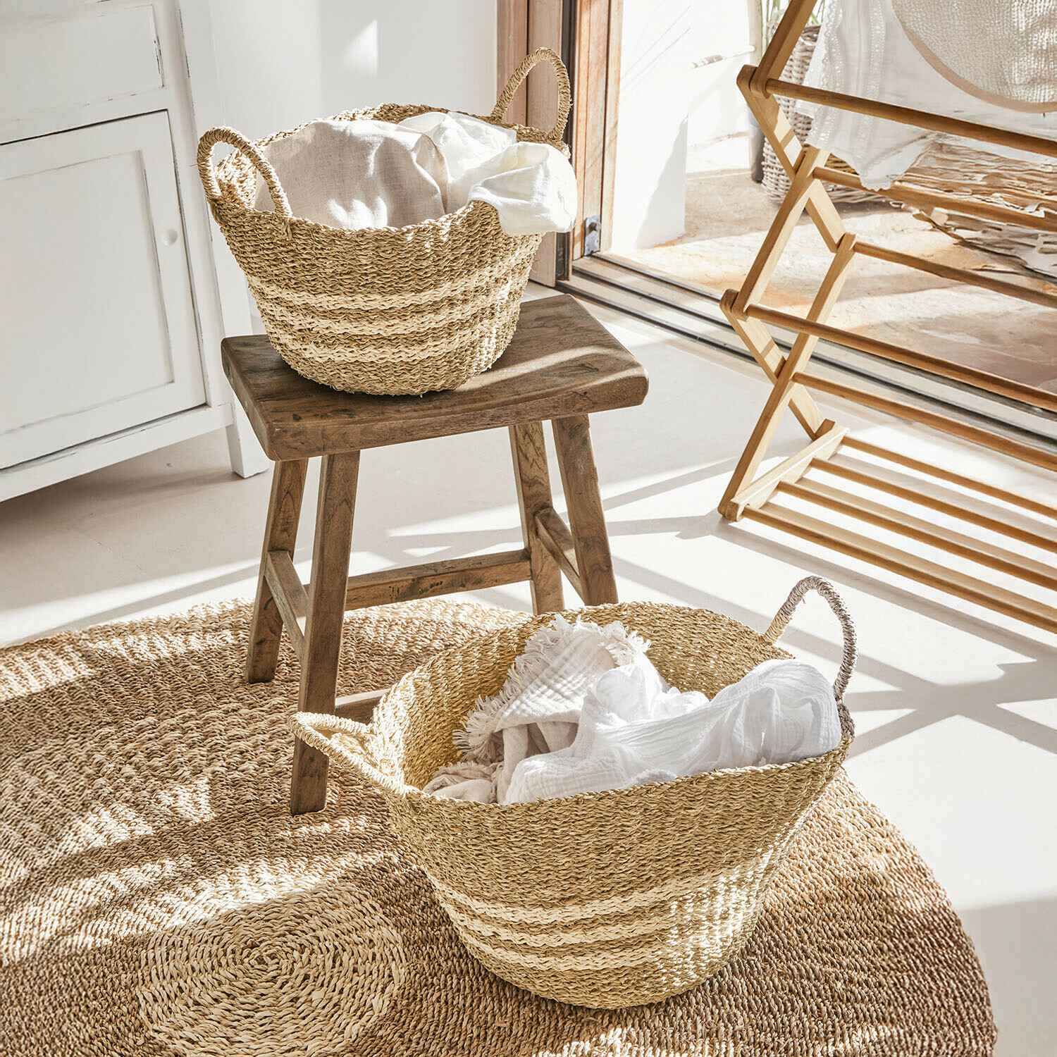 Naturfarbene Seegras-Körbe mit weißen Stoffen auf rundem Teppich in hellem Raum