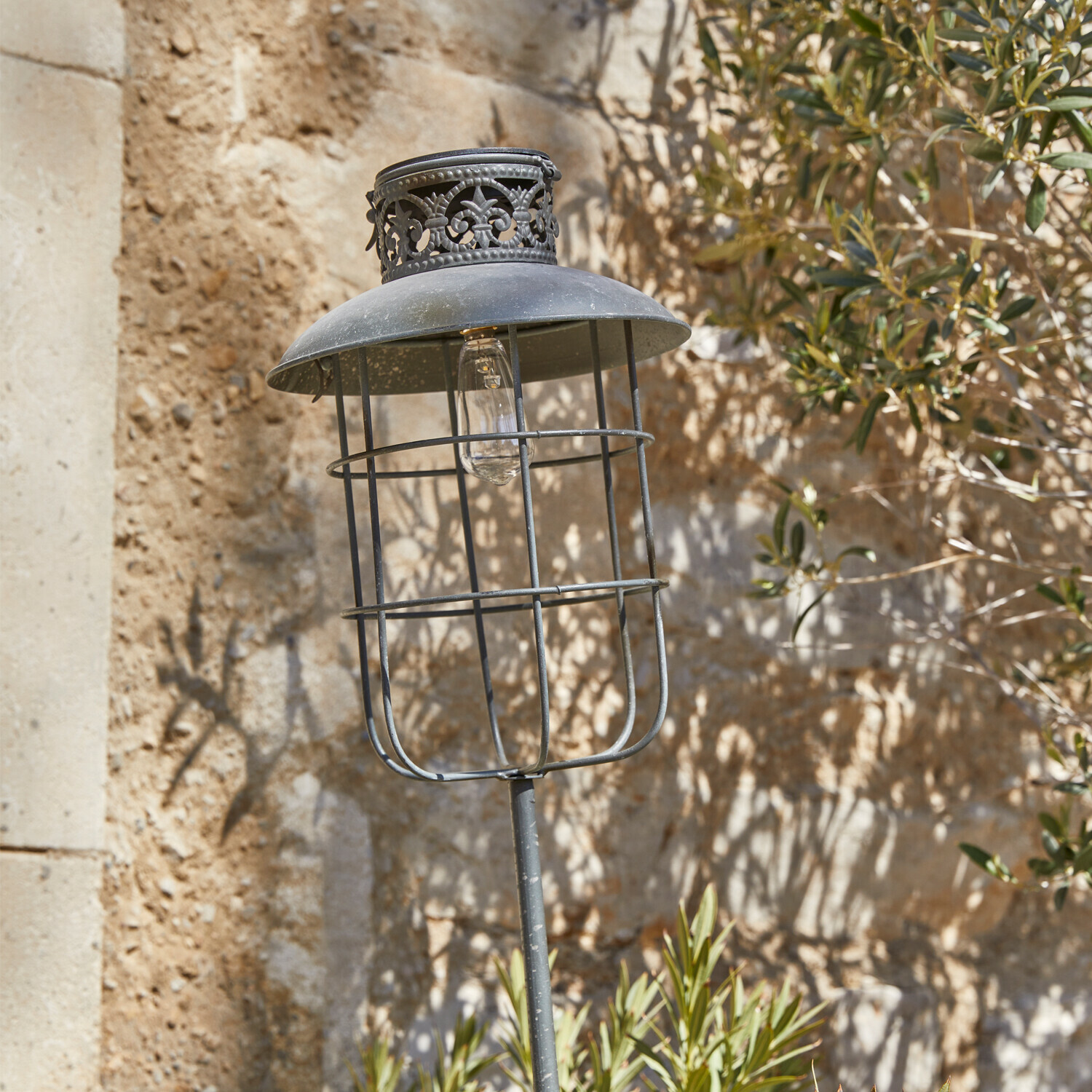 Metall-Gartenlampe im Vintage-Stil mit schwarzem Schirm und dekorativem Muster vor Steinmauer