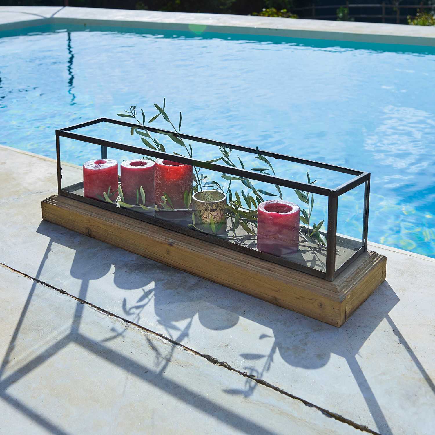 Glasdekoration mit Metallrahmen und Holzsockel, rote Kerzen und grüne Zweige innen