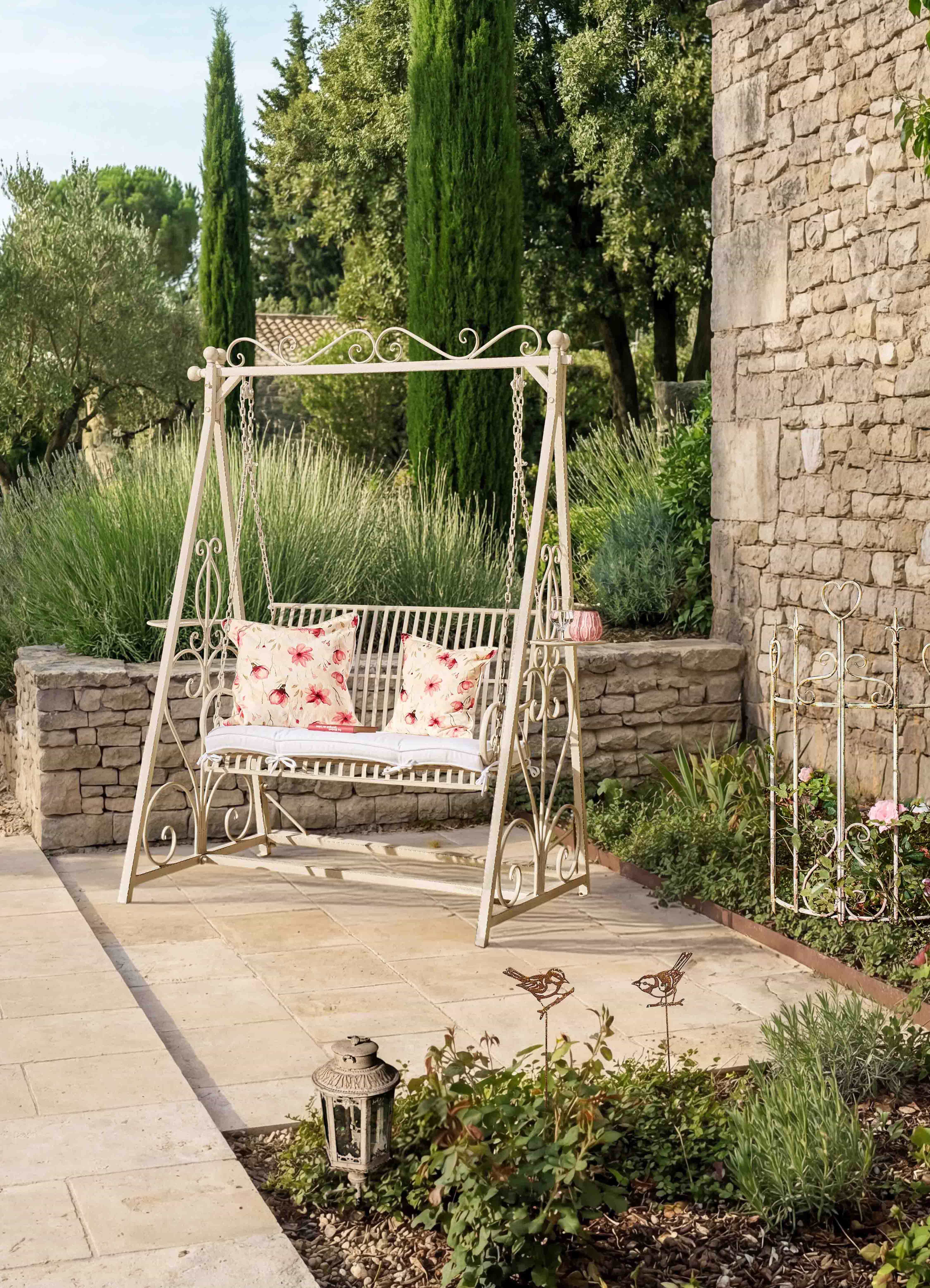 Metall-Gartenschaukel in Creme mit floralen Kissen auf Terrasse mit Natursteinmauer