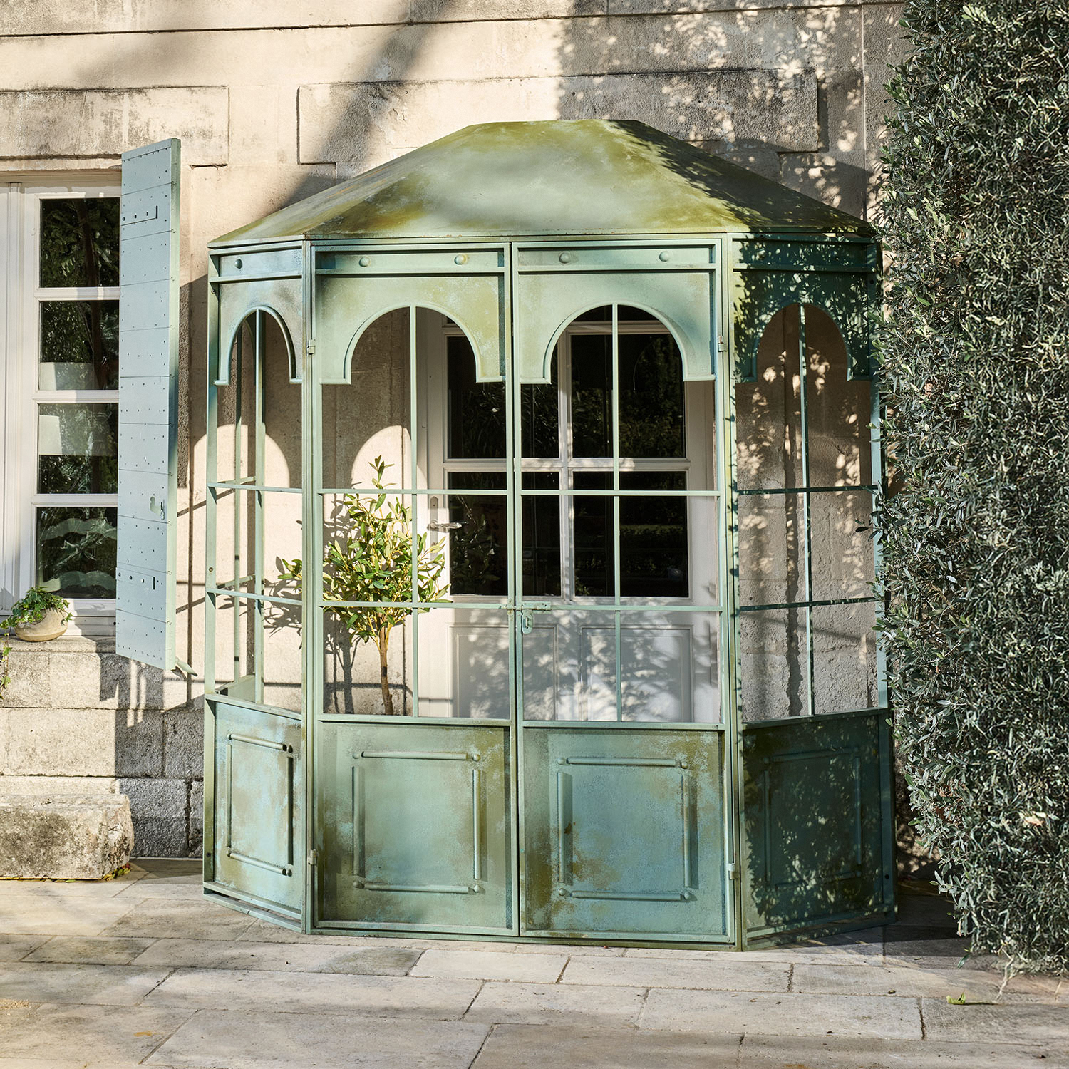 Grüne Metall-Gartenlaube mit verglasten Paneelen und dekorativen Bögen auf Steinterrasse
