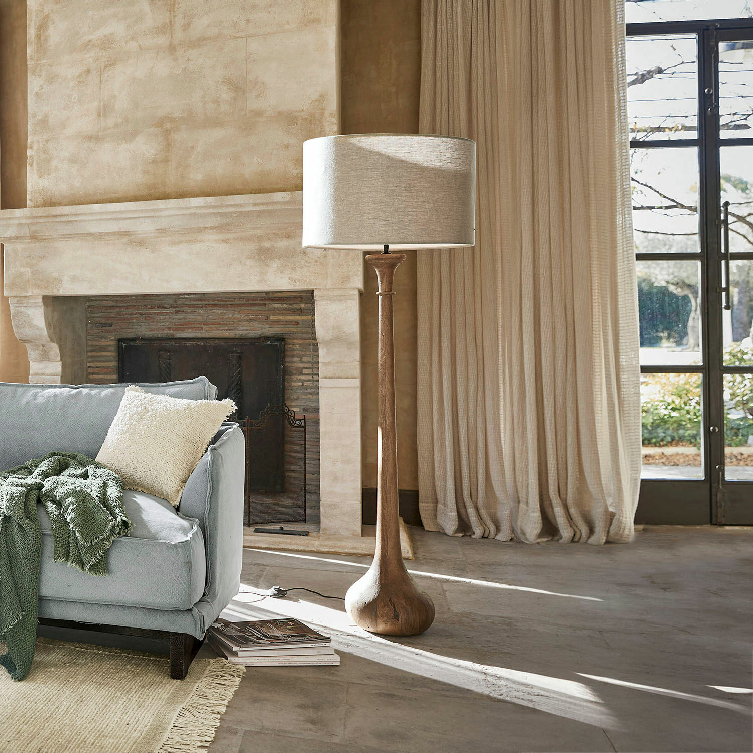 Stehlampe mit Holzfuß und hellem Lampenschirm im gemütlichen Wohnzimmer mit Kamin und Sofa