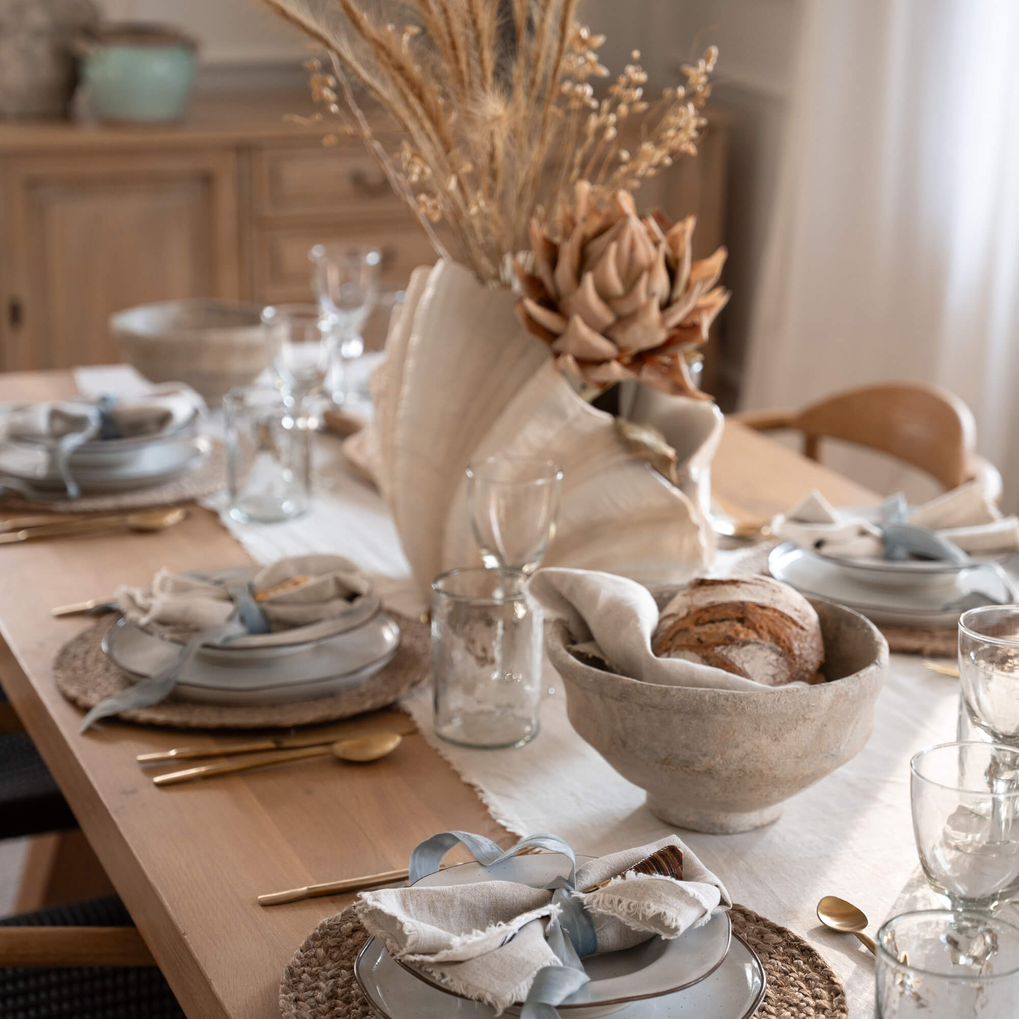 Rustikaler Holztisch mit natürlichem Läufer, Keramiktellern und getrockneten Blumen als Dekoration