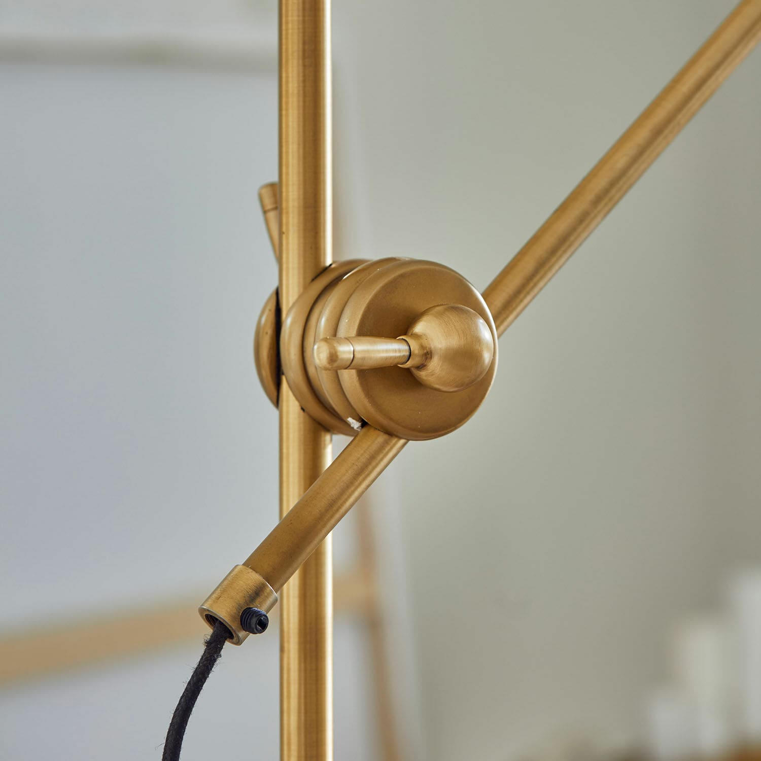 Goldfarbener Metallarm einer Lampe mit verstellbarem Gelenk und schwarzem Kabel, modernes Beleuchtungsdesign