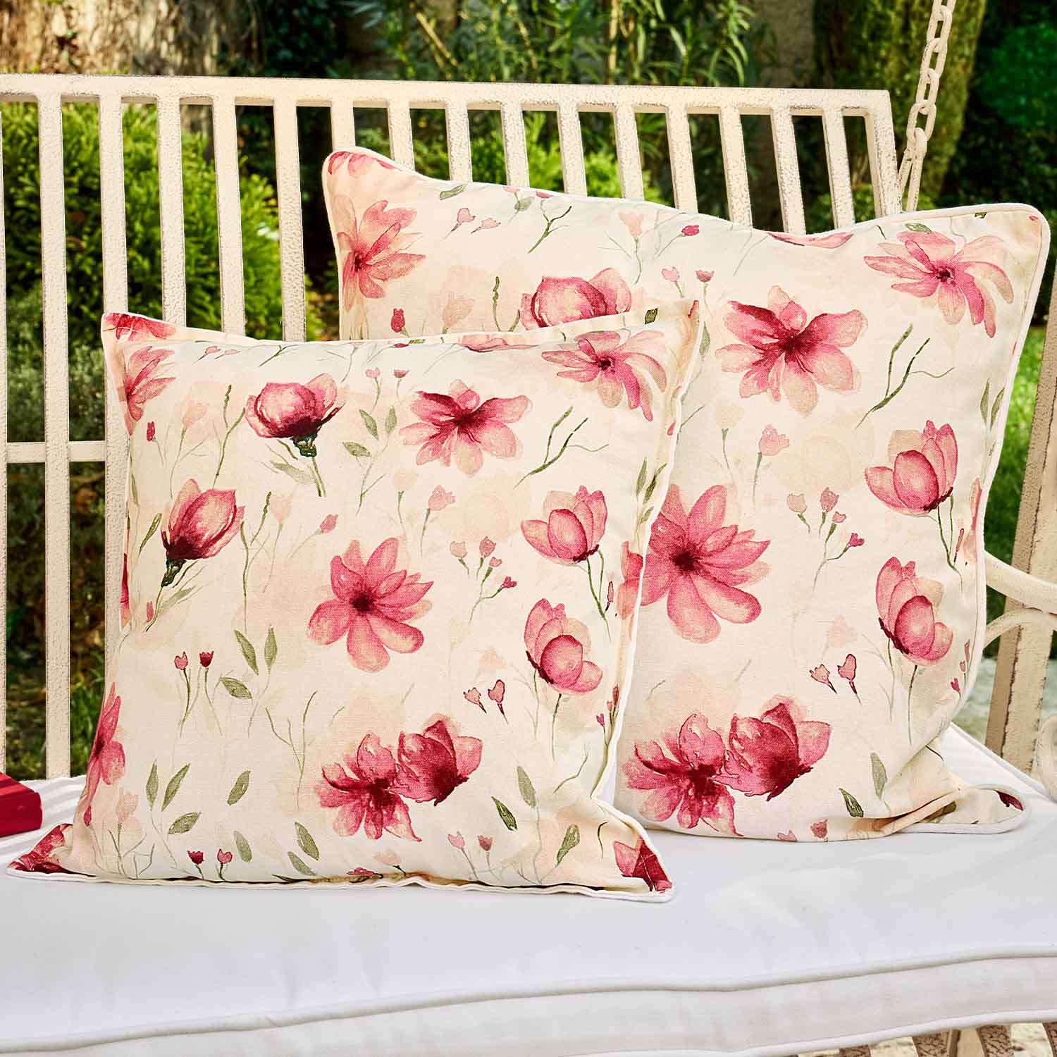 Zwei quadratische Baumwollkissen in Creme mit rosa Blumenmuster, ideal für Gartenmöbel