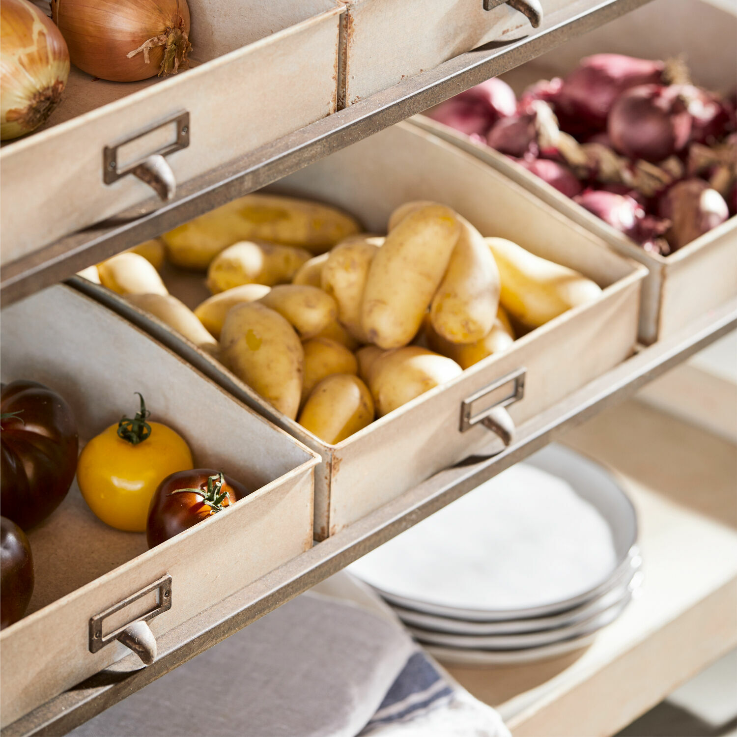 Metallboxen mit Zwiebeln, Kartoffeln und Tomaten in einer hellen Küche