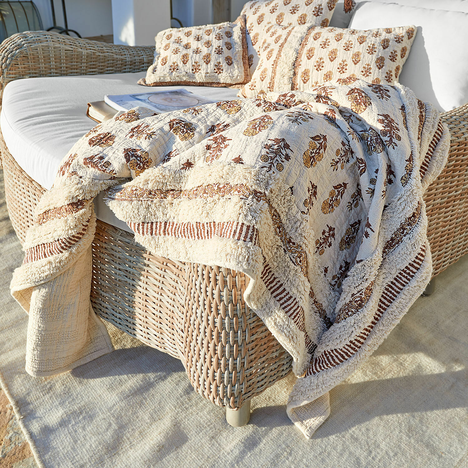 Plaid Arsalan Beige Baumwolldecke und Kissen mit braunem Muster auf Rattansofa auf Terrasse