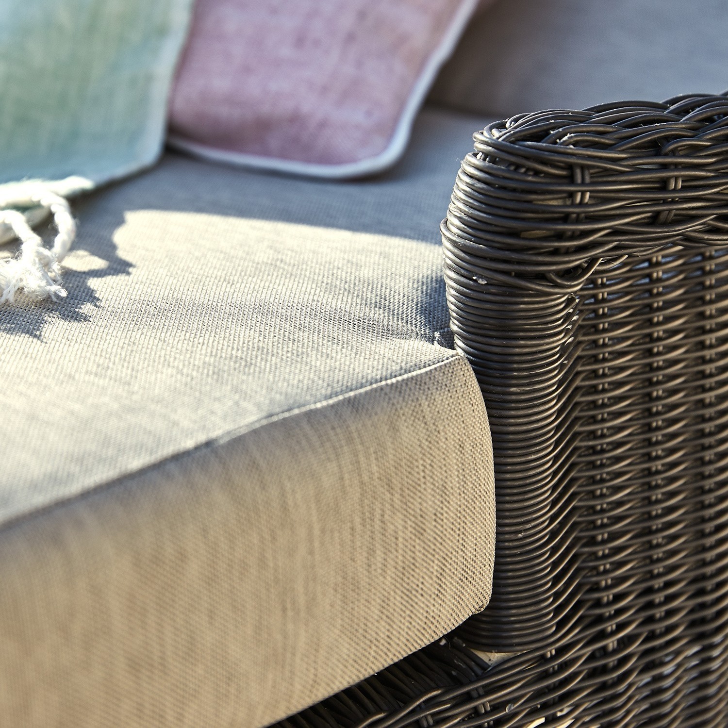 Dunkles Rattan-Sofa mit hellgrauem Stoffpolster und pastellfarbenen Kissen für gemütliche Sitzfläche