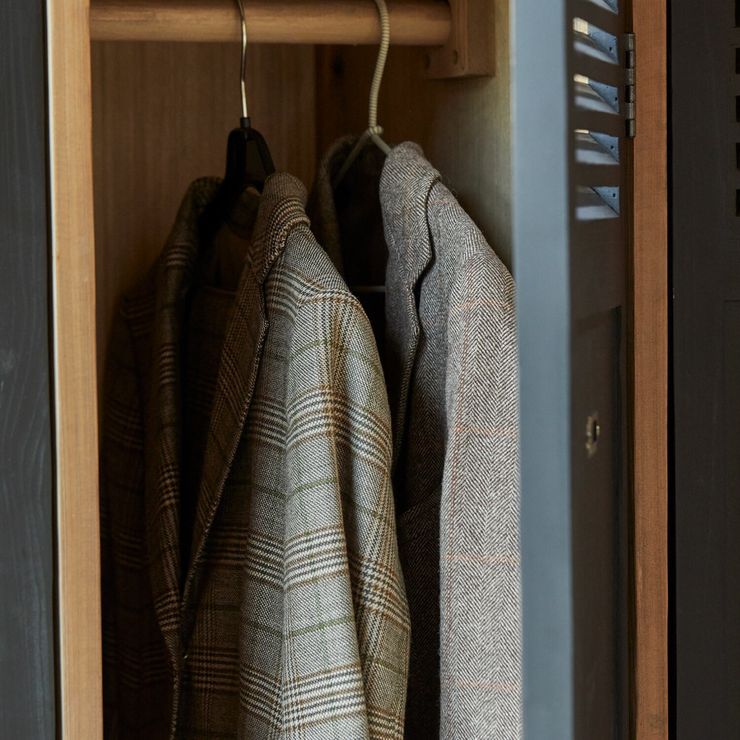 Graue und braune karierte Blazer an Kleiderbügeln in einem Holzschrank hängend
