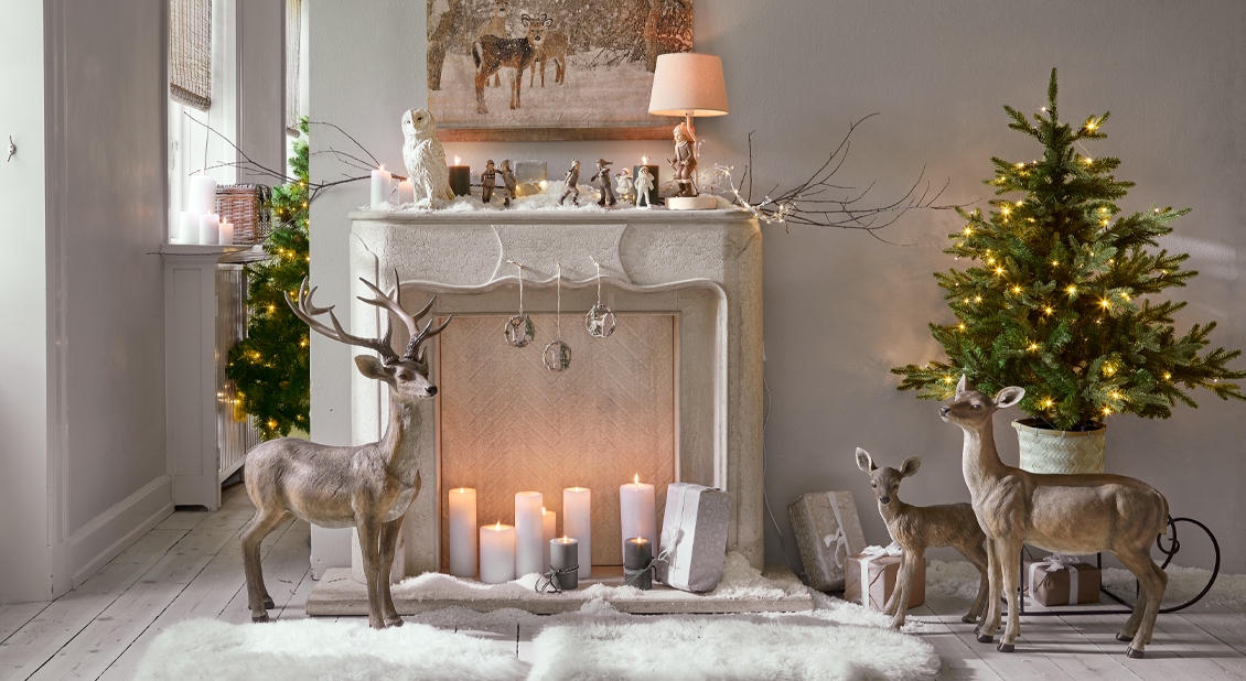 Weiße Steinkaminkonsole mit Weihnachtsdekoration und Hirschfiguren in gemütlichem Raum