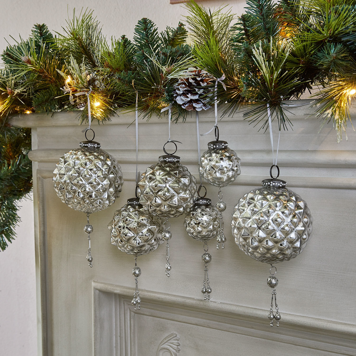 Weihnachtsschmuck 6er Set Murron Silberne Glas-Weihnachtskugeln mit Anhängern vor Kamin und grünen Zweigen mit Lichterkette