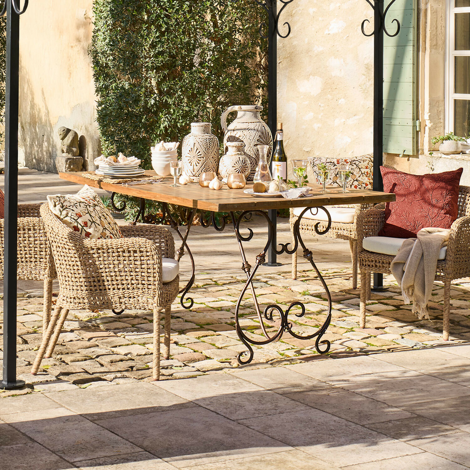 Gartentisch mit Holzplatte und Metallbeinen, Rattanstühle mit Kissen und Keramikdekorationen im Freien