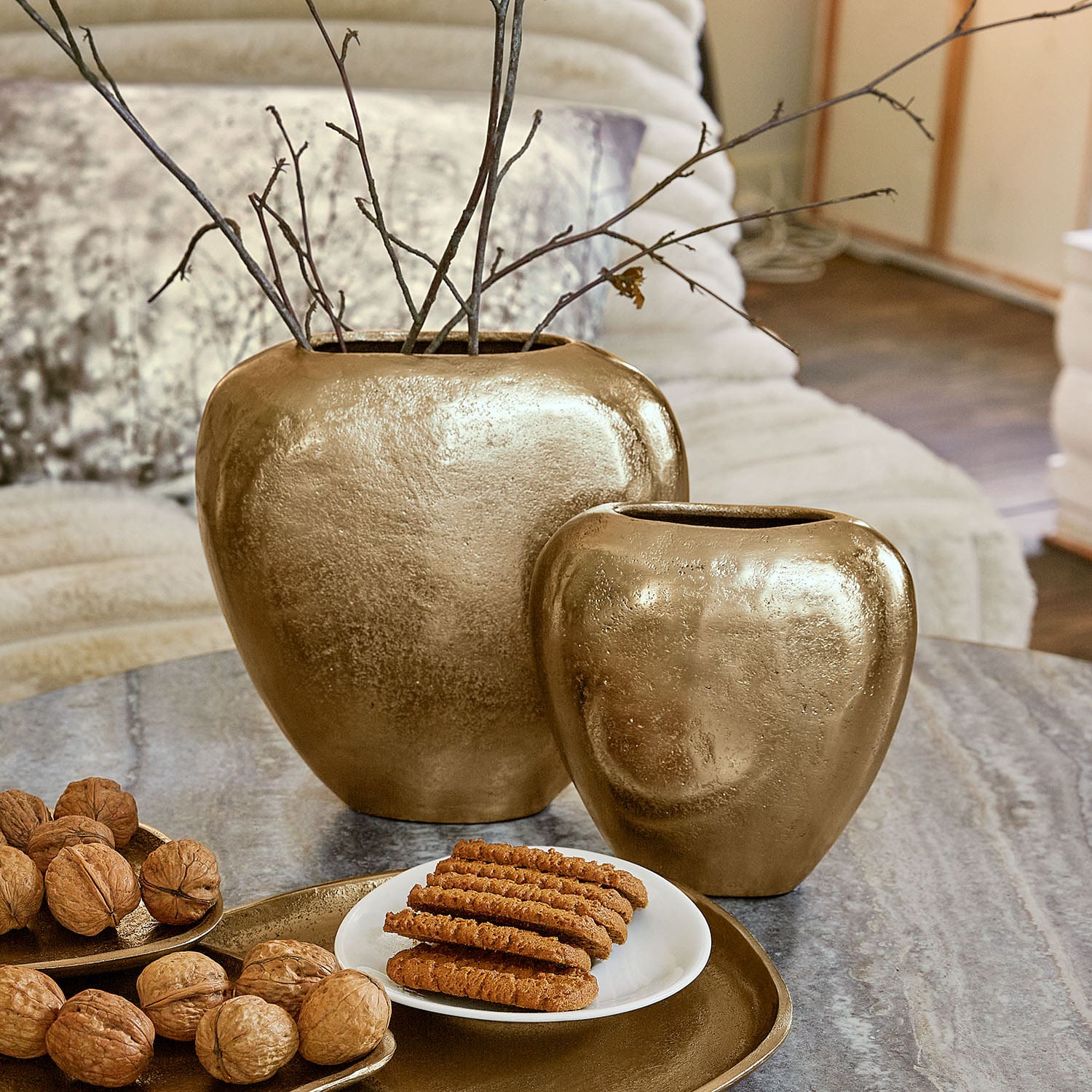Set aus zwei goldfarbenen Keramikvasen auf Tisch mit Walnüssen und Keksen, Wohnaccessoire