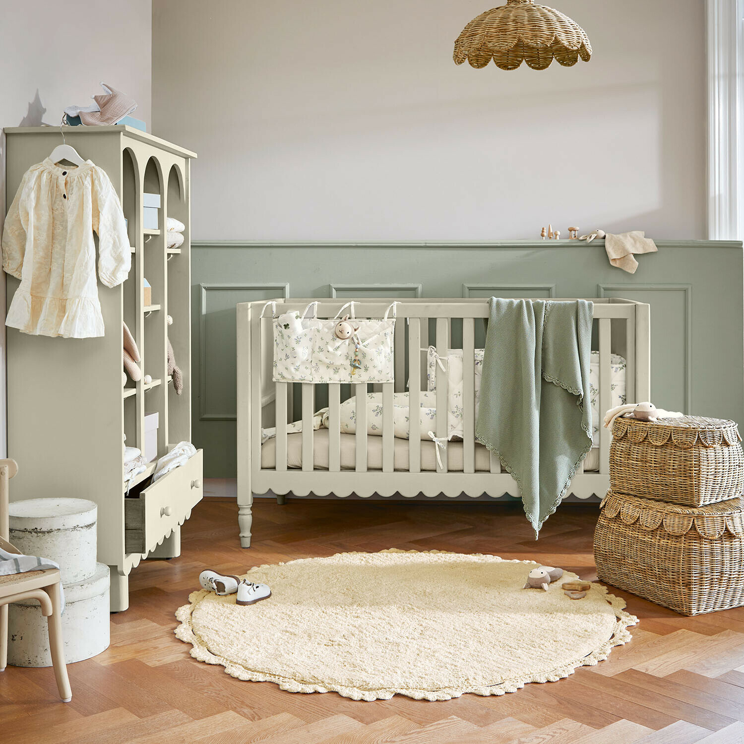 Gemütliches Kinderzimmer mit beige Babybett, grünem Decke und zwei geflochtenen Körben auf Holzboden
