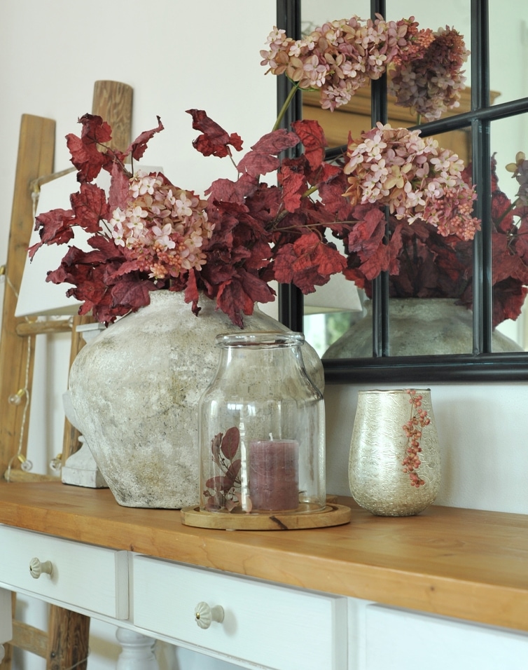 Dekorativer Steinvase mit roten Blättern und rosa Blüten auf Holztisch im Wohnzimmer