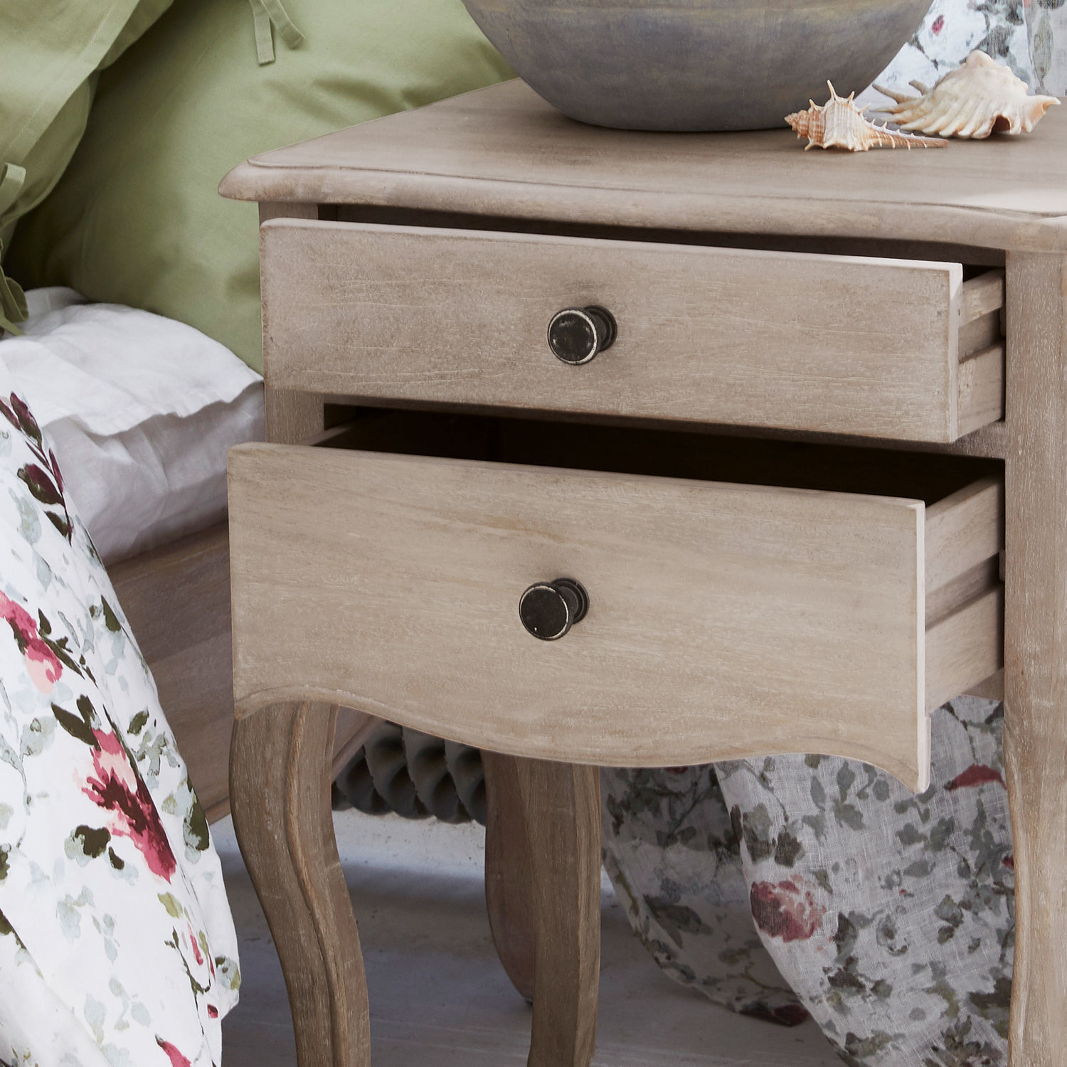 Helle Holz-Nachttisch mit zwei Schubladen und Metallgriffen neben Bett mit Blumenbettwäsche