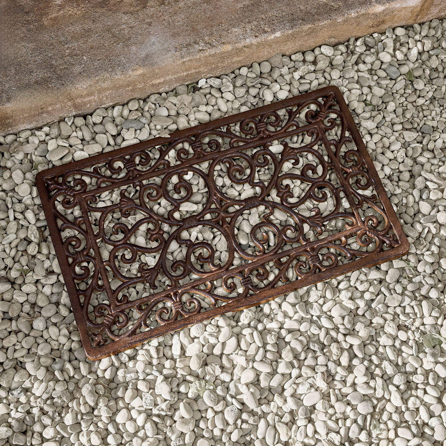 Braune Metallmatte mit dekorativem Muster auf weißen Steinen, gusseiserne Fußmatte